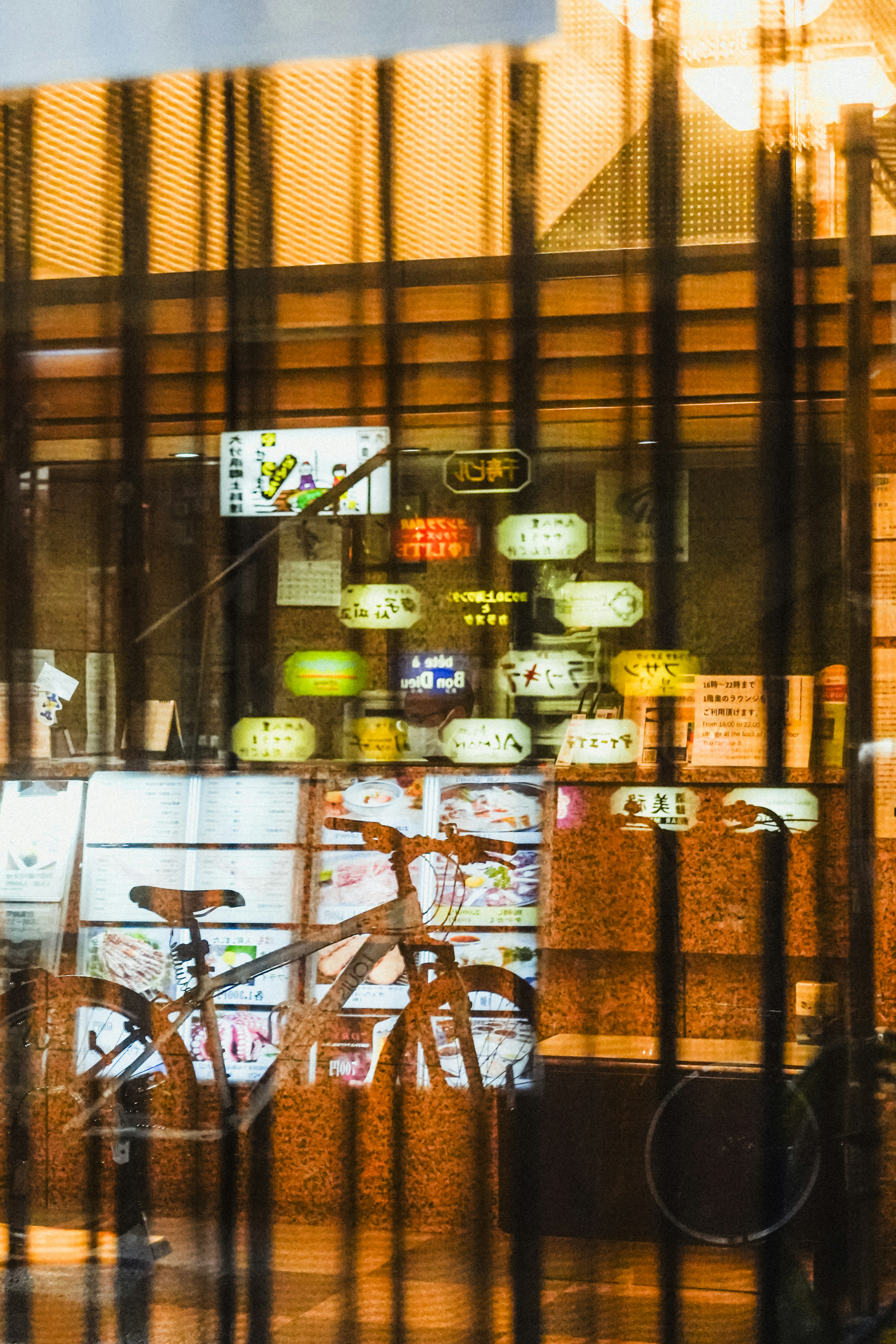 View through a window showing a bicycle and bright signs inside a restaurant