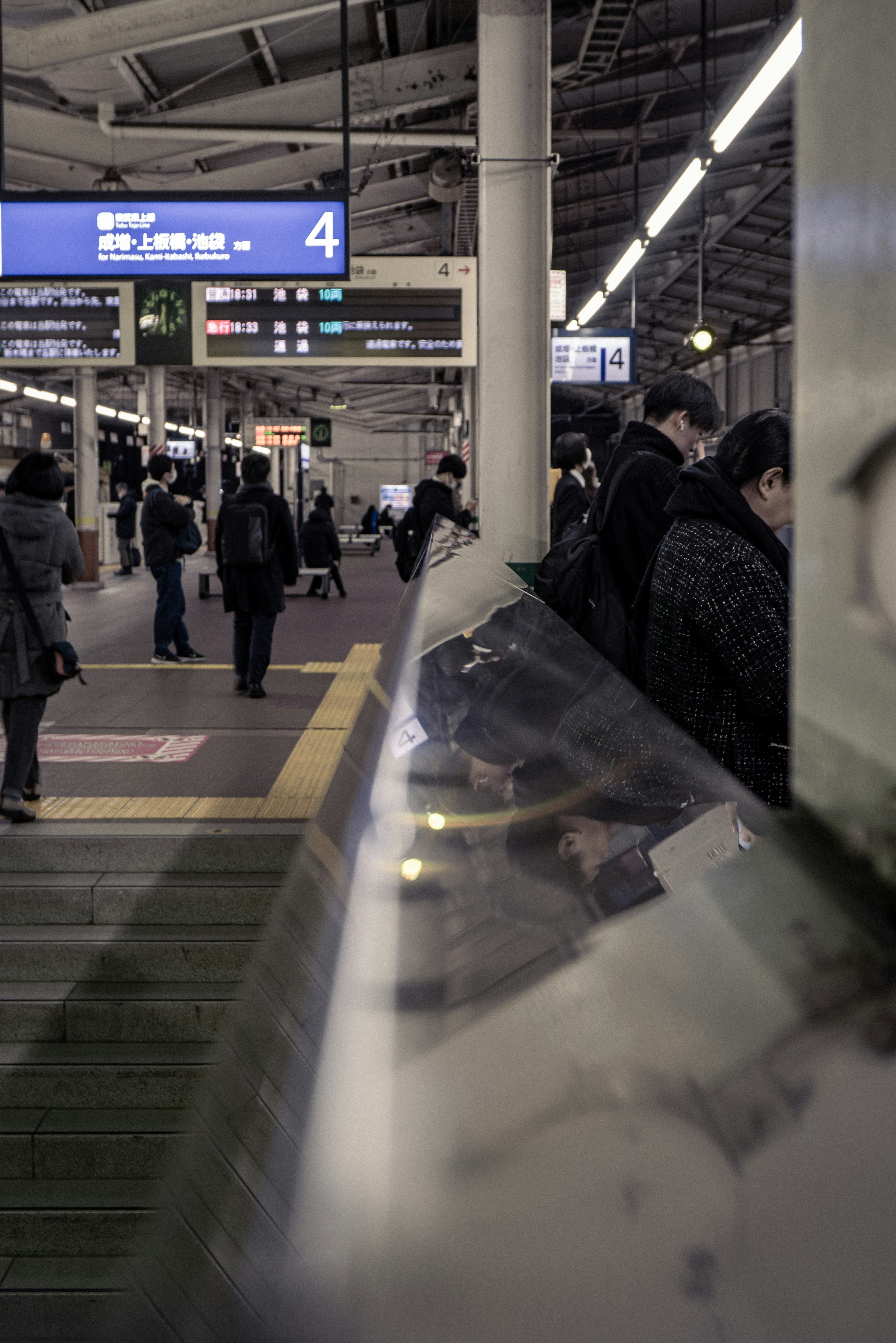 駅のプラットフォームで人々が待っている様子と看板が見える