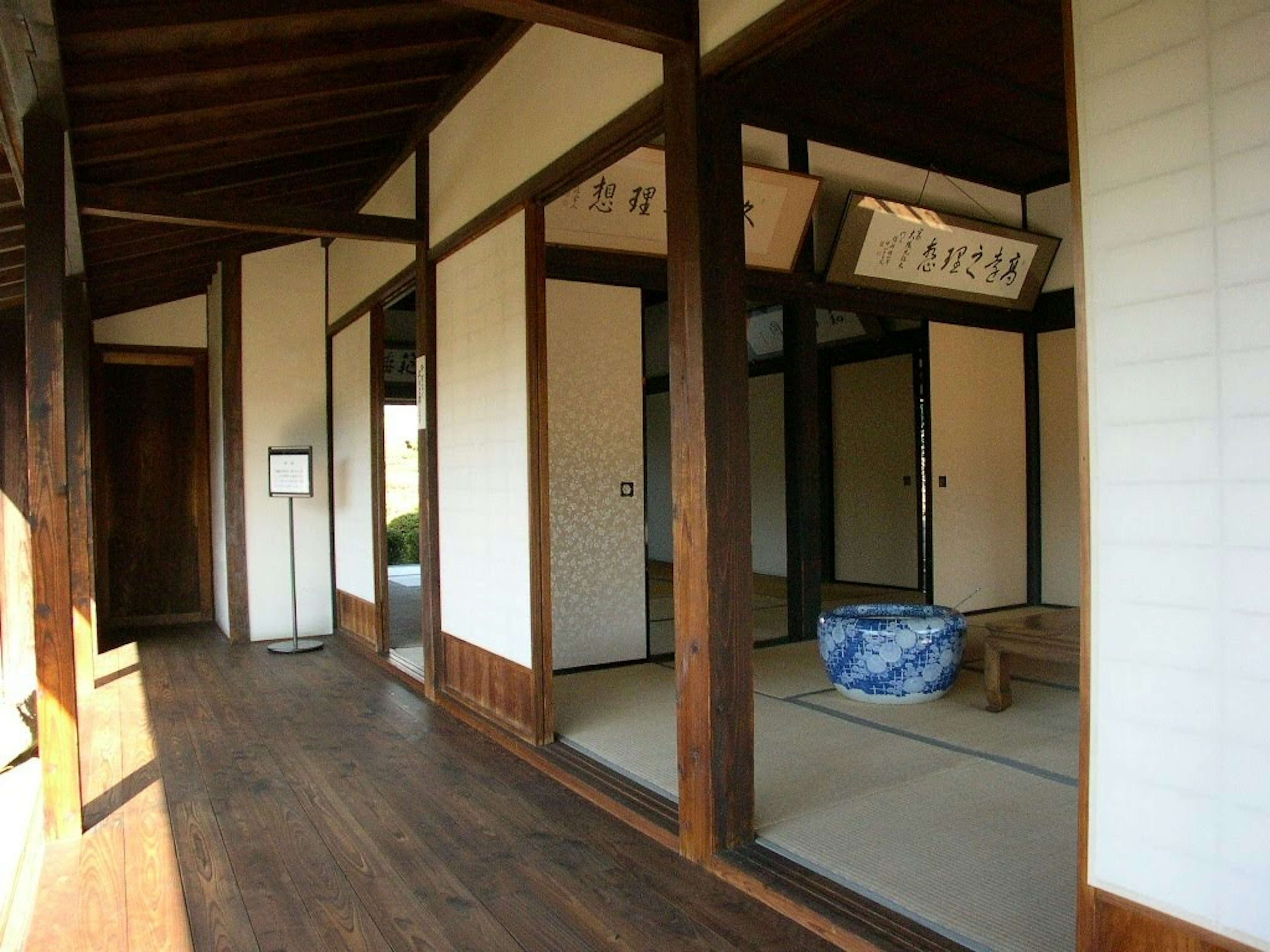 Koridor rumah tradisional Jepang dengan lantai kayu dan layar shoji, bantal biru diletakkan di dalam ruangan