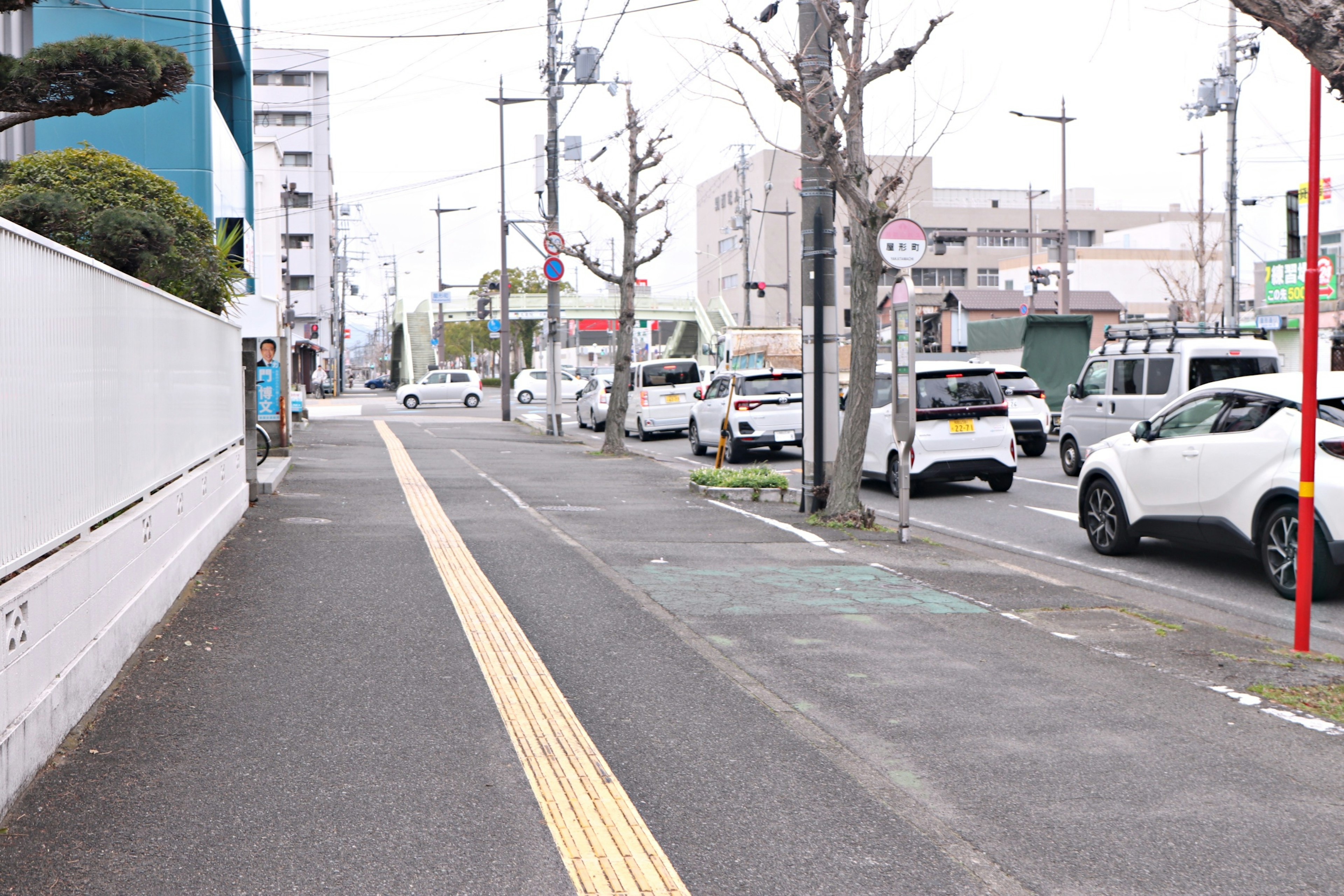 静かな街の通りが映る画像 歩道には黄色いガイドラインがあり 車が停まっている