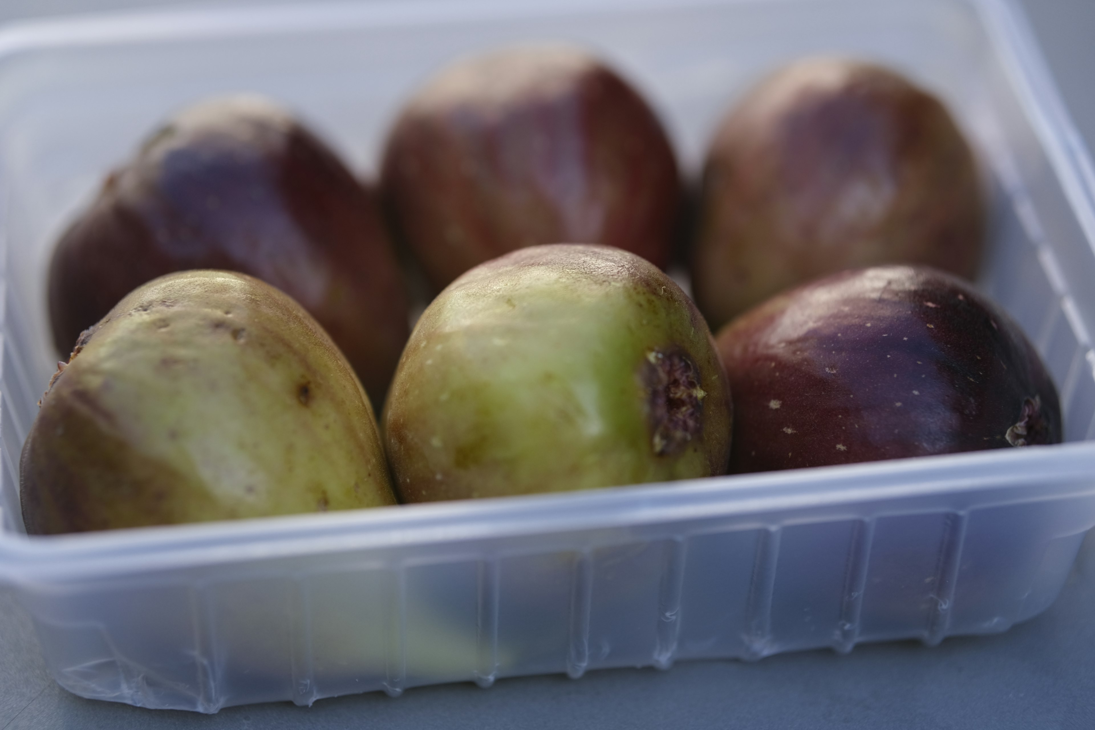 Seis frutas en un recipiente transparente con una mezcla de colores verdes y púrpuras