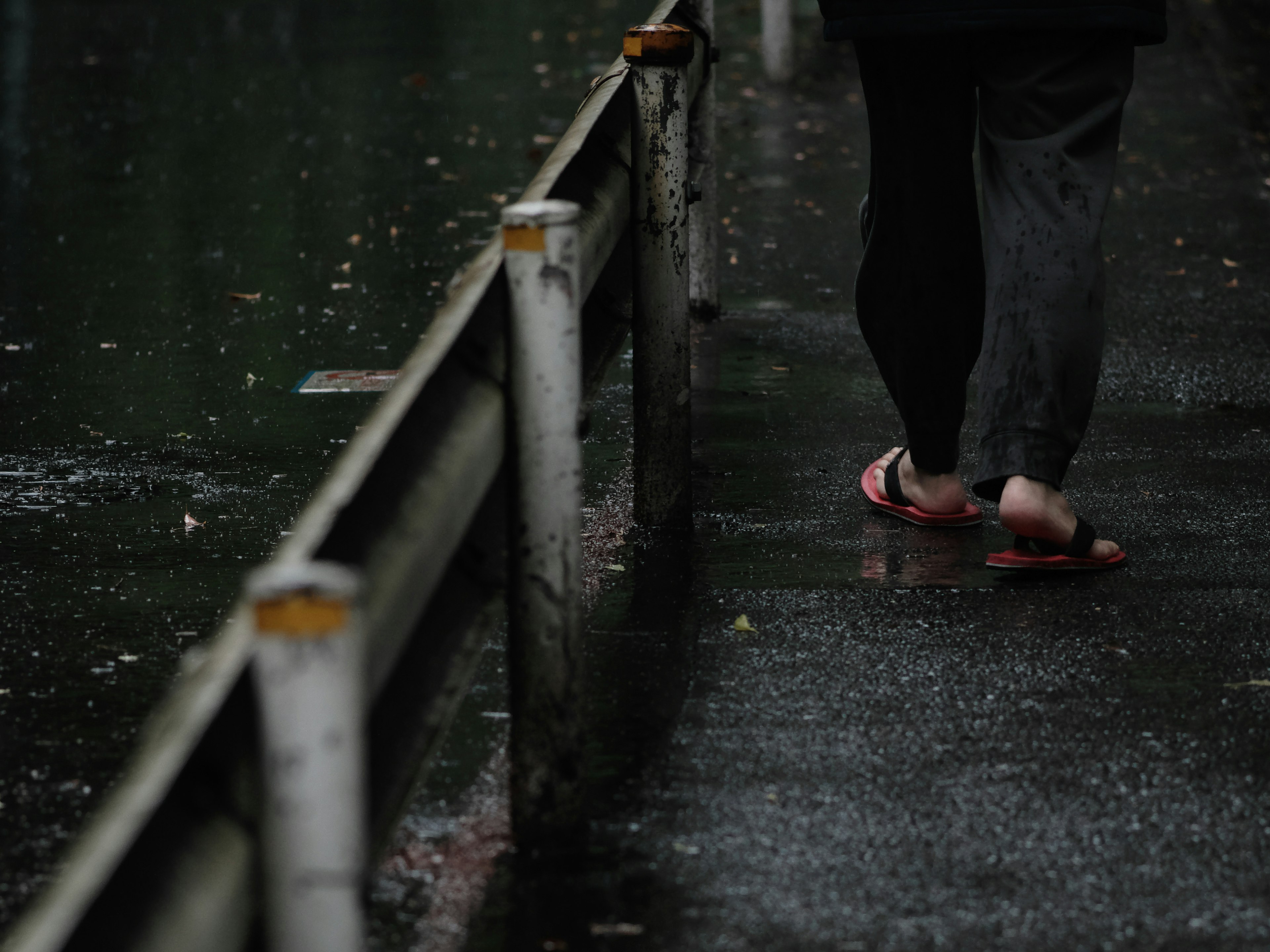 Person, der auf einem nassen Bürgersteig mit Flip-Flops im Regen geht