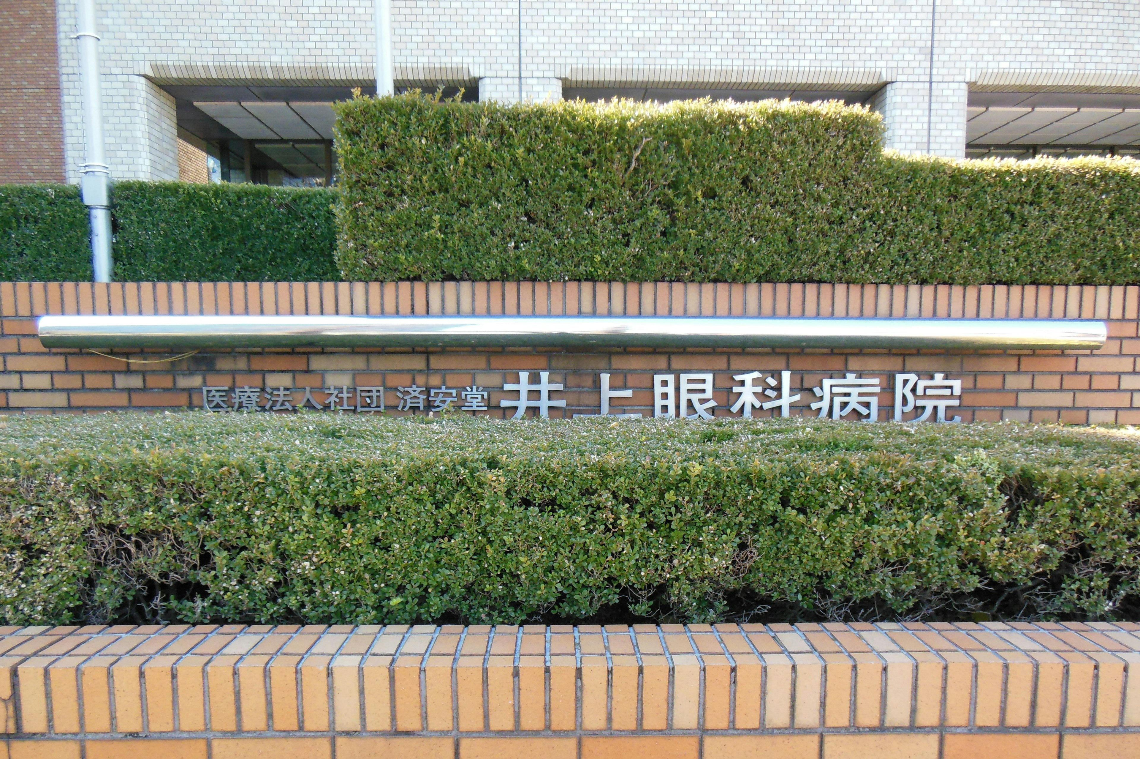 Schild des Inoue Augenklinik vor einer grünen Hecke