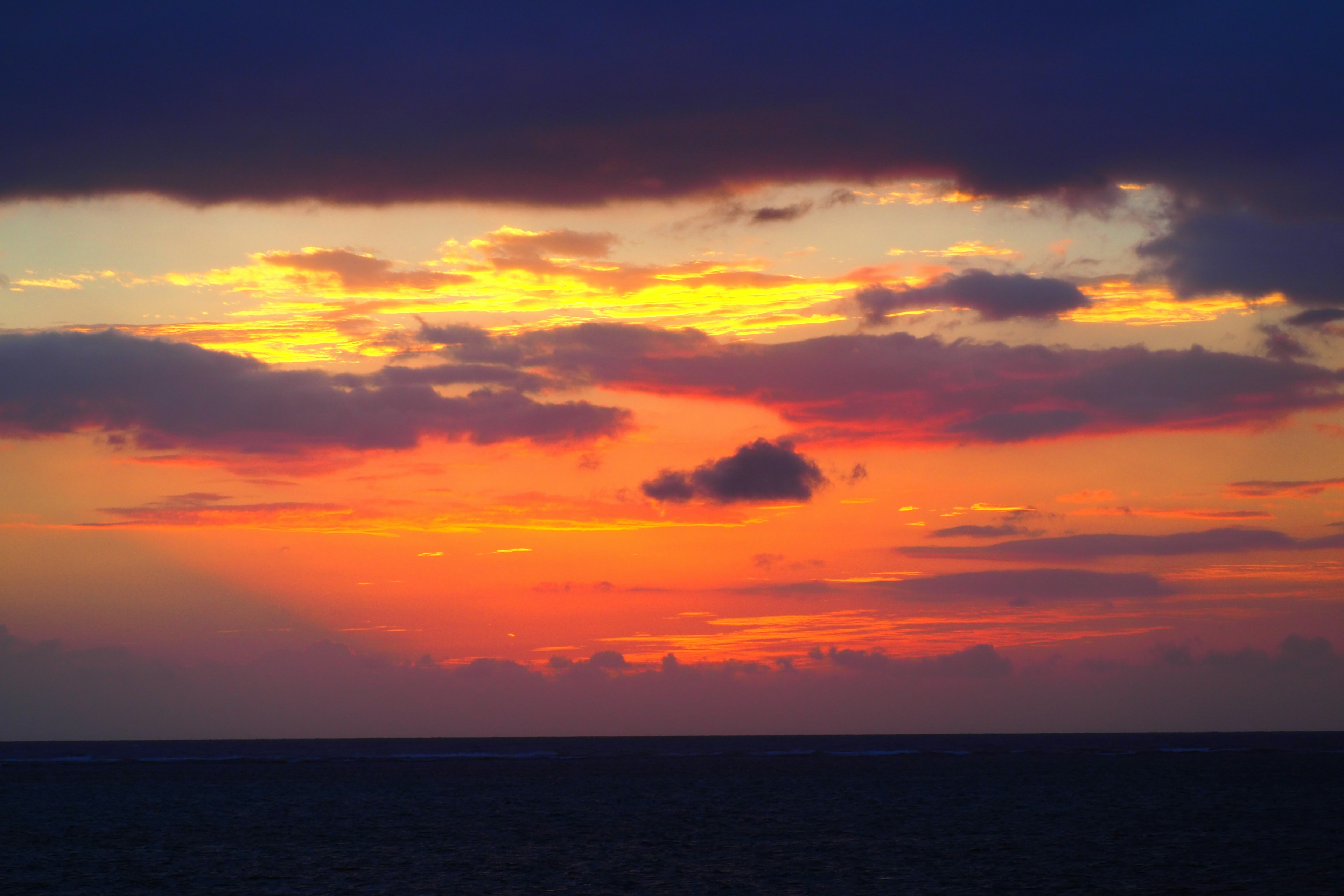 Atardecer vibrante sobre el océano con tonos naranjas y morados y nubes en silueta