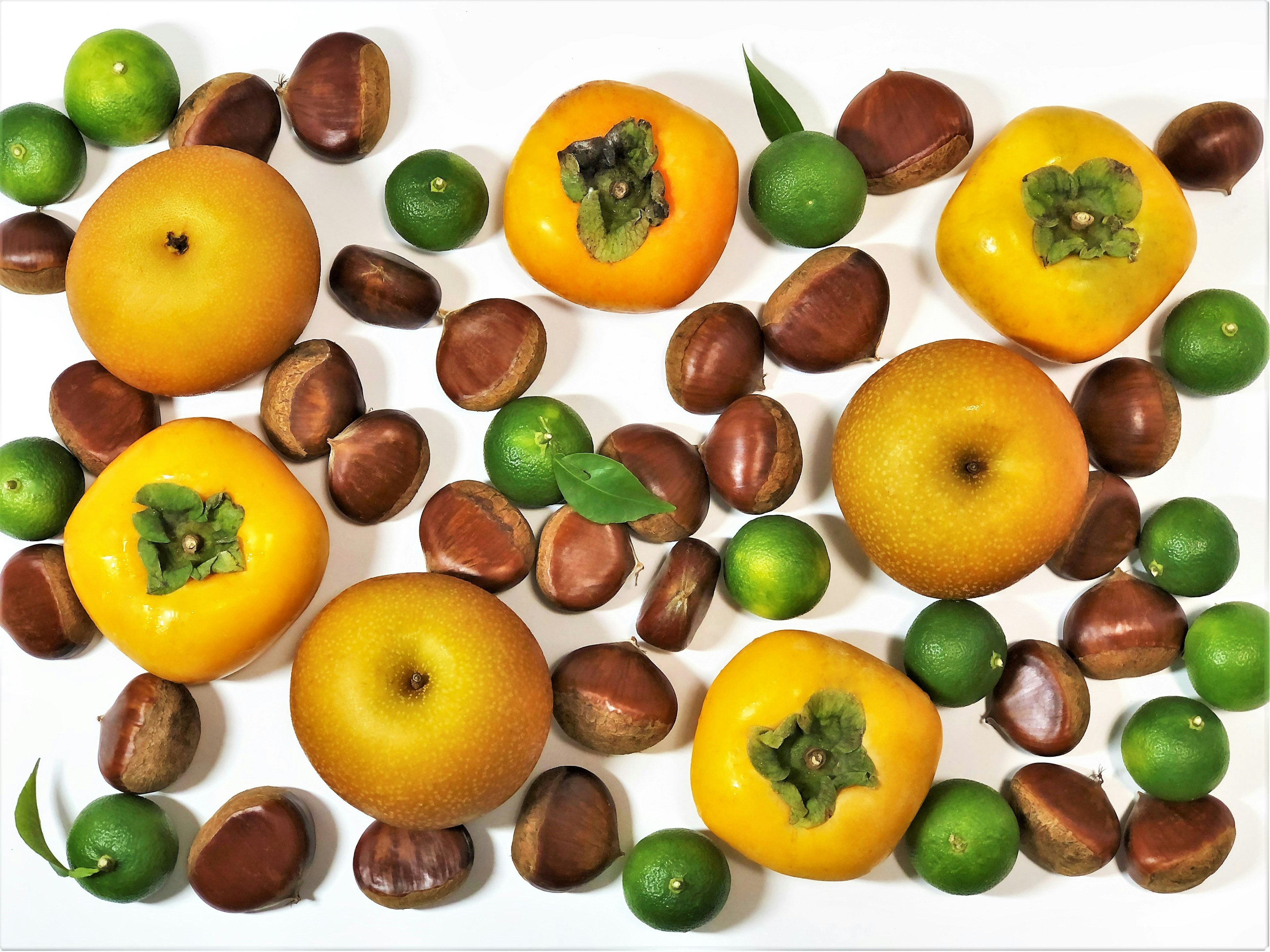 Arrangement of yellow persimmons and green citrus fruits on a white background