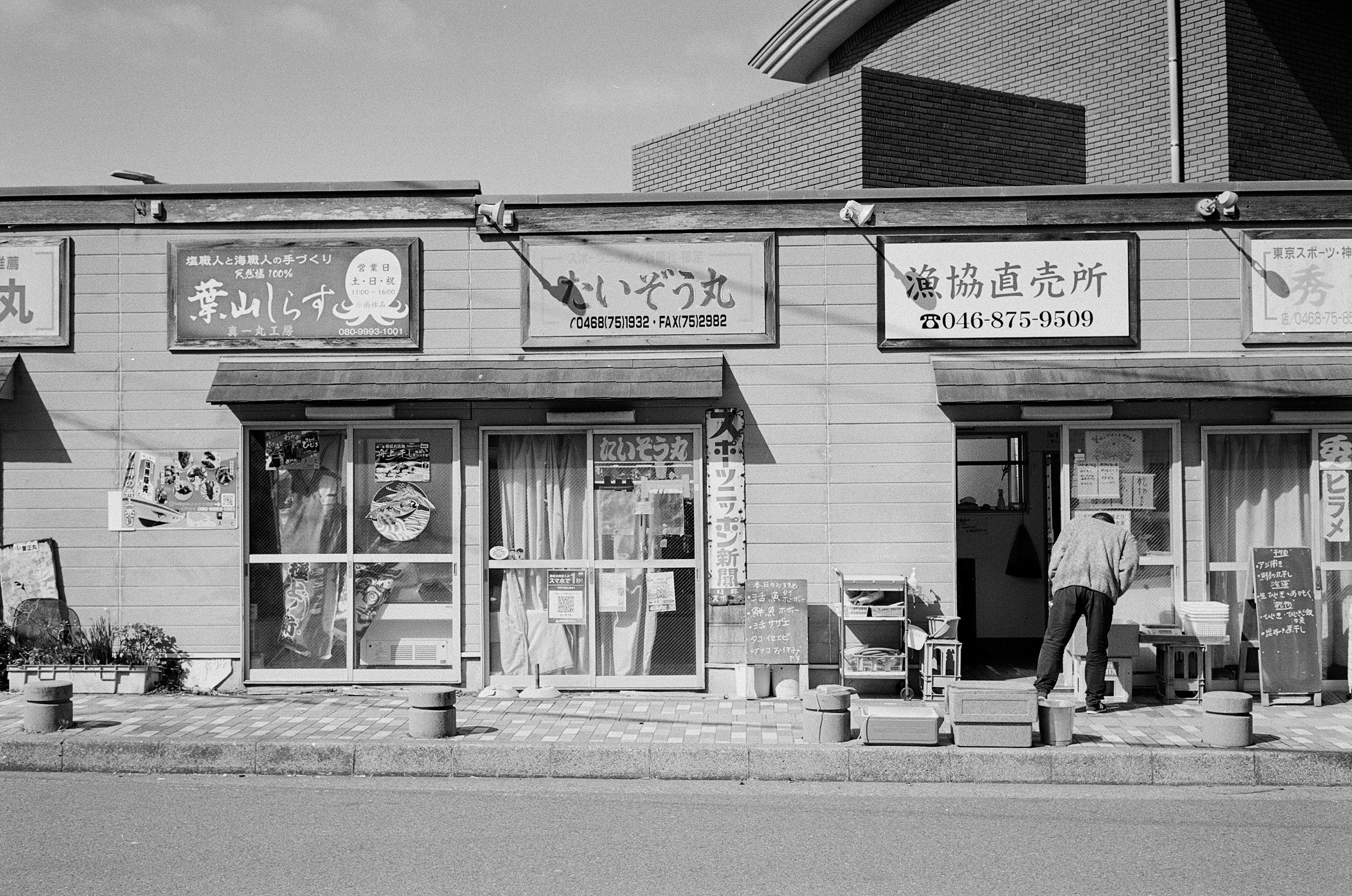 Black and white street scene with storefronts and a person working