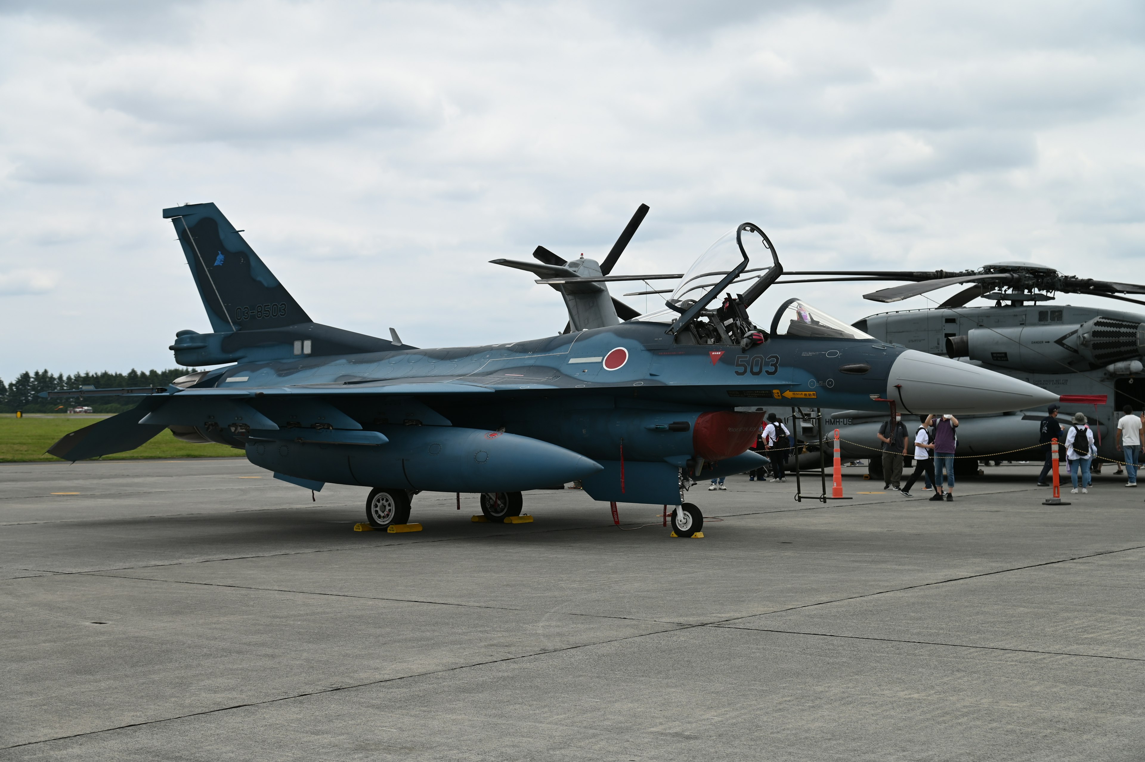 A blue aircraft on the runway with people and a helicopter nearby