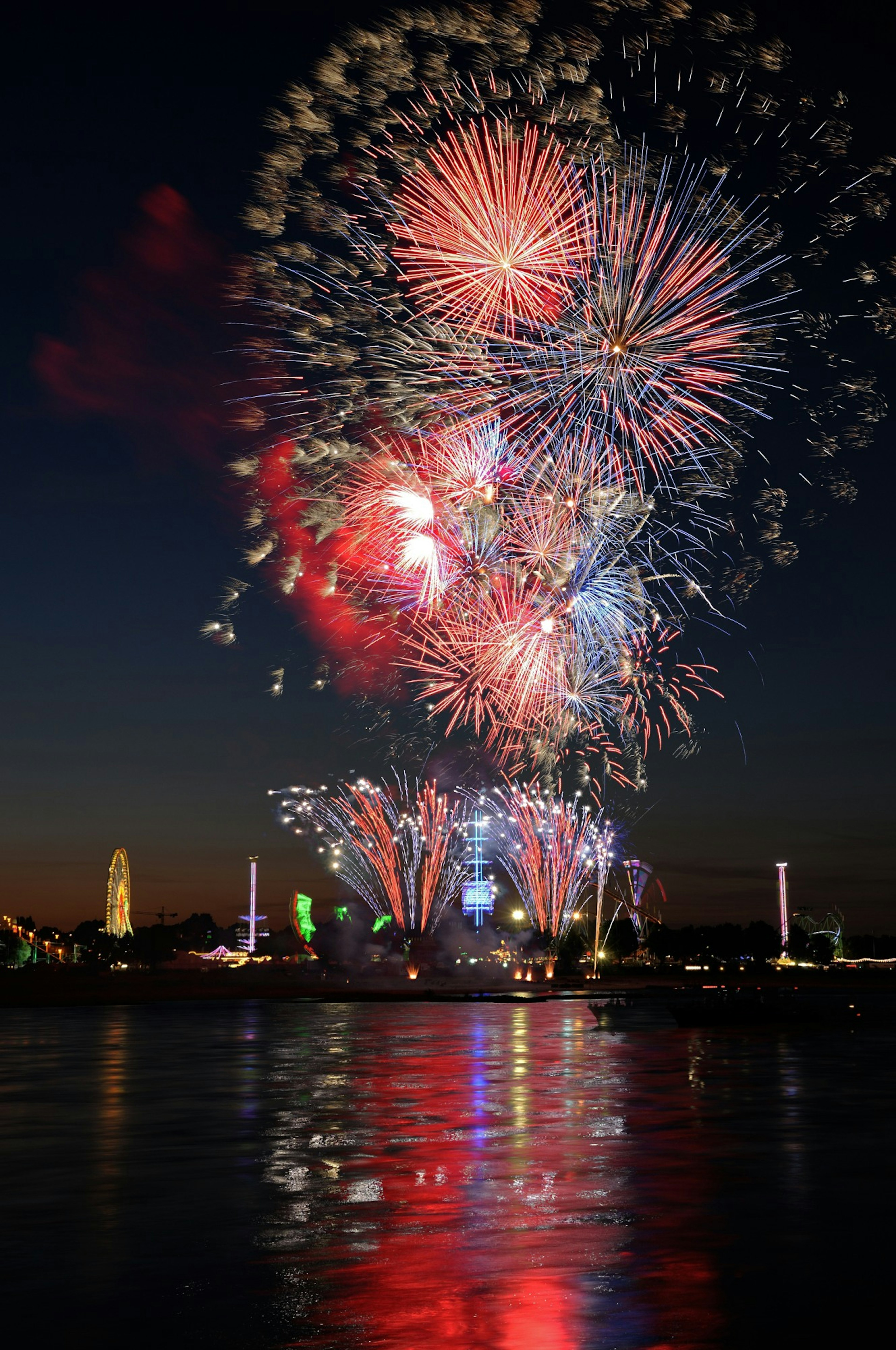 Spettacolo di fuochi d'artificio colorati sopra l'acqua di notte che si riflettono sulla superficie