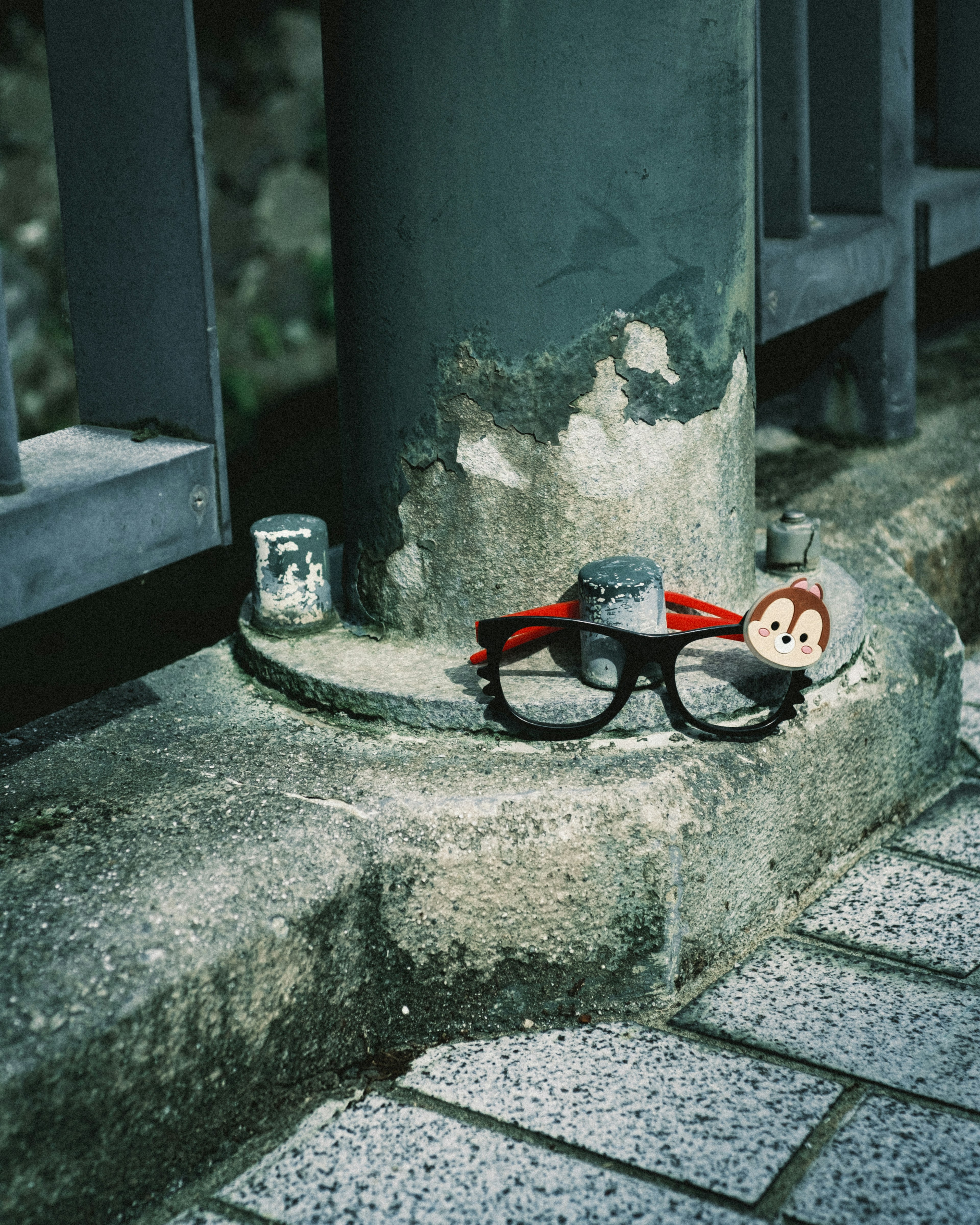 Glasses with a red band and a small character placed at the corner of a concrete structure