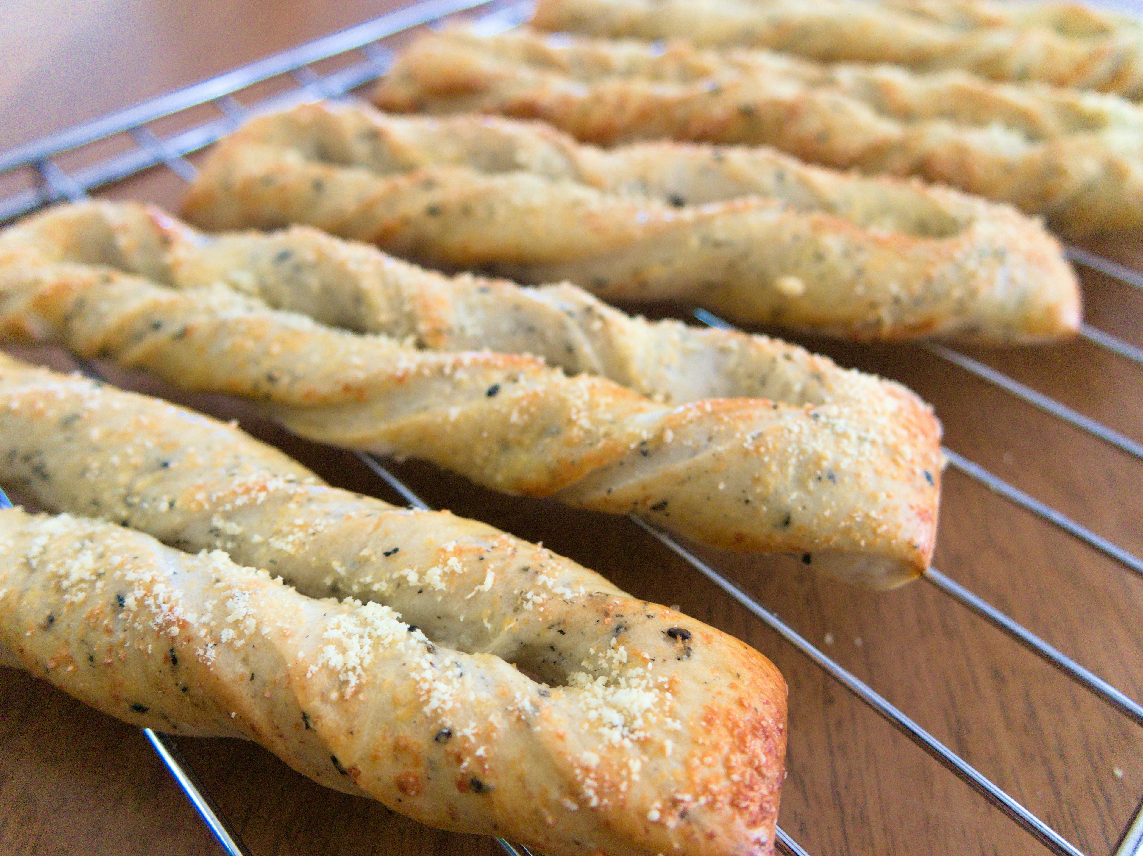 Bastoncini di pane attorcigliati appena sfornati disposti su una griglia