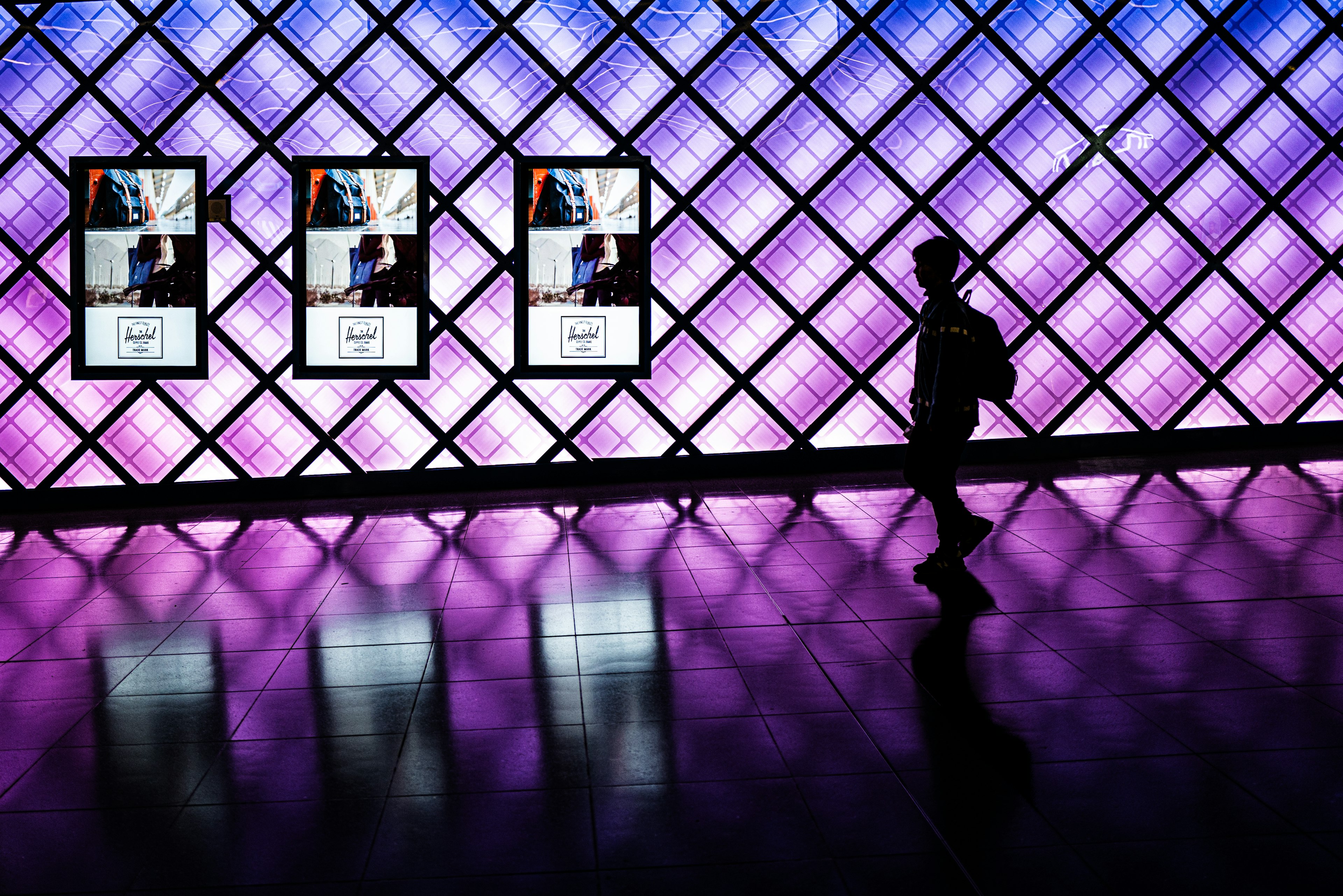 Silhouette einer Person, die vor einer Wand mit lila und blauer Beleuchtung und digitalen Panels geht