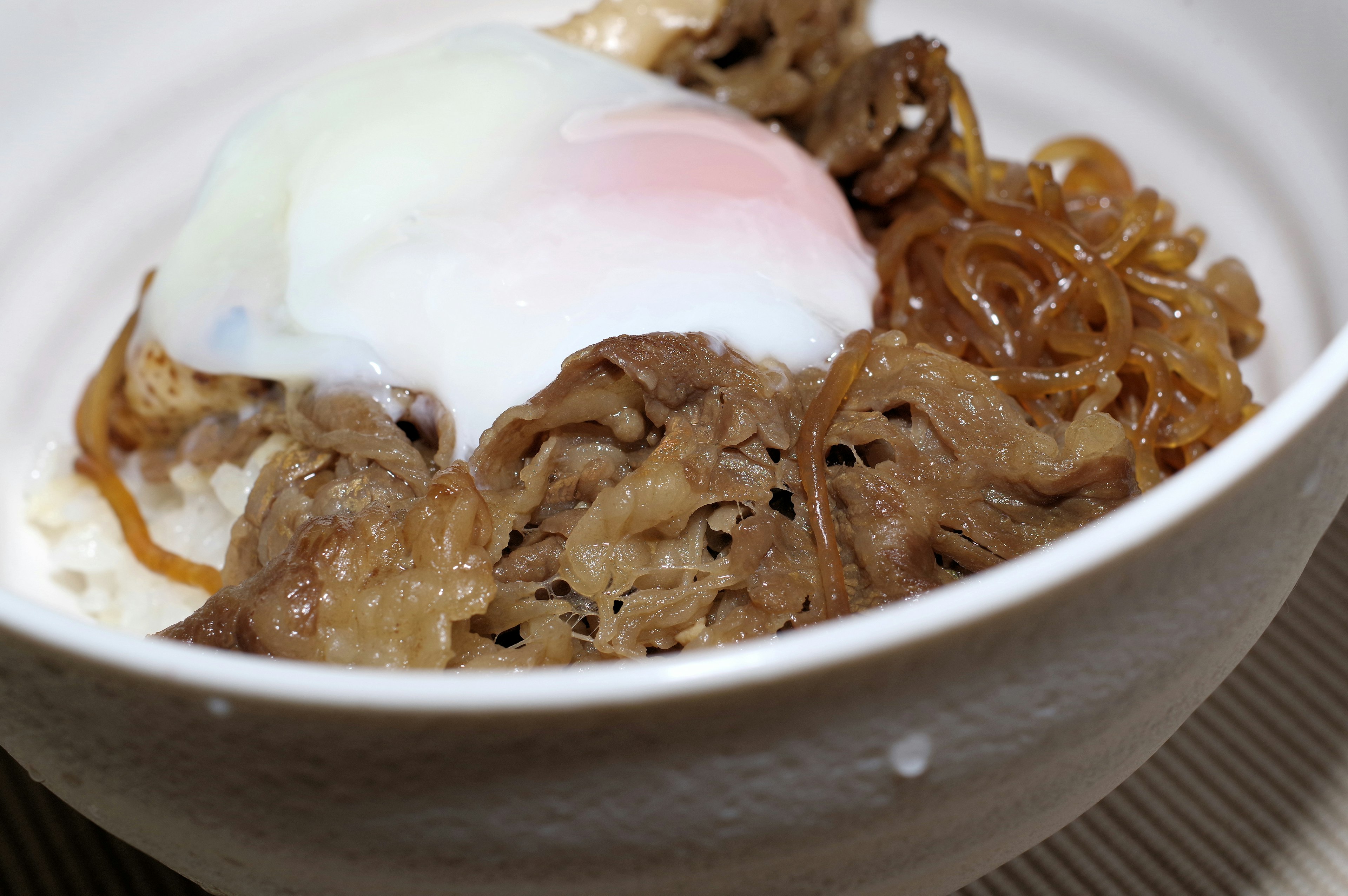 Bowl of gyudon topped with a poached egg and noodles