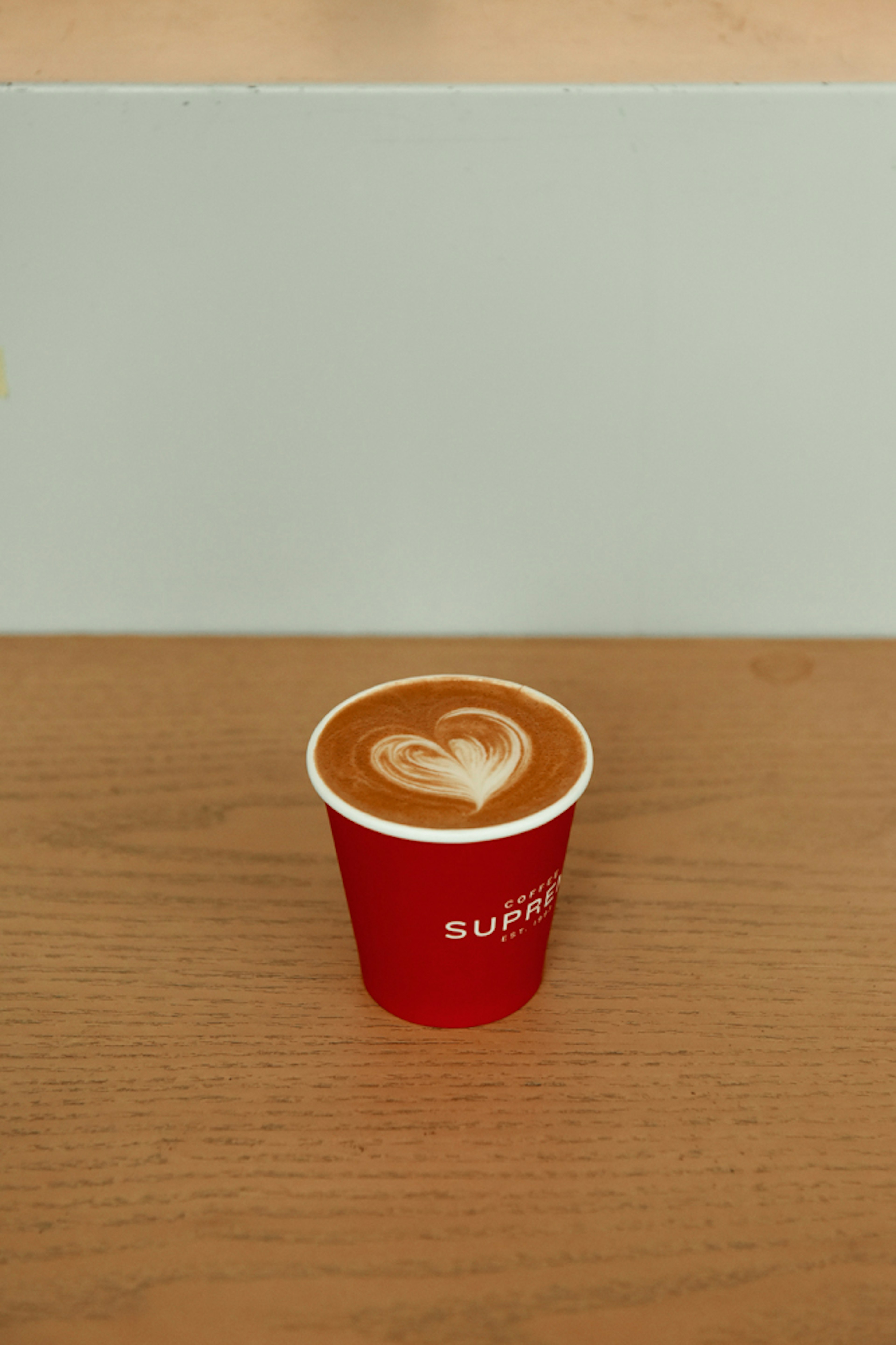 Café con arte latte en forma de corazón en una taza roja sobre una mesa de madera