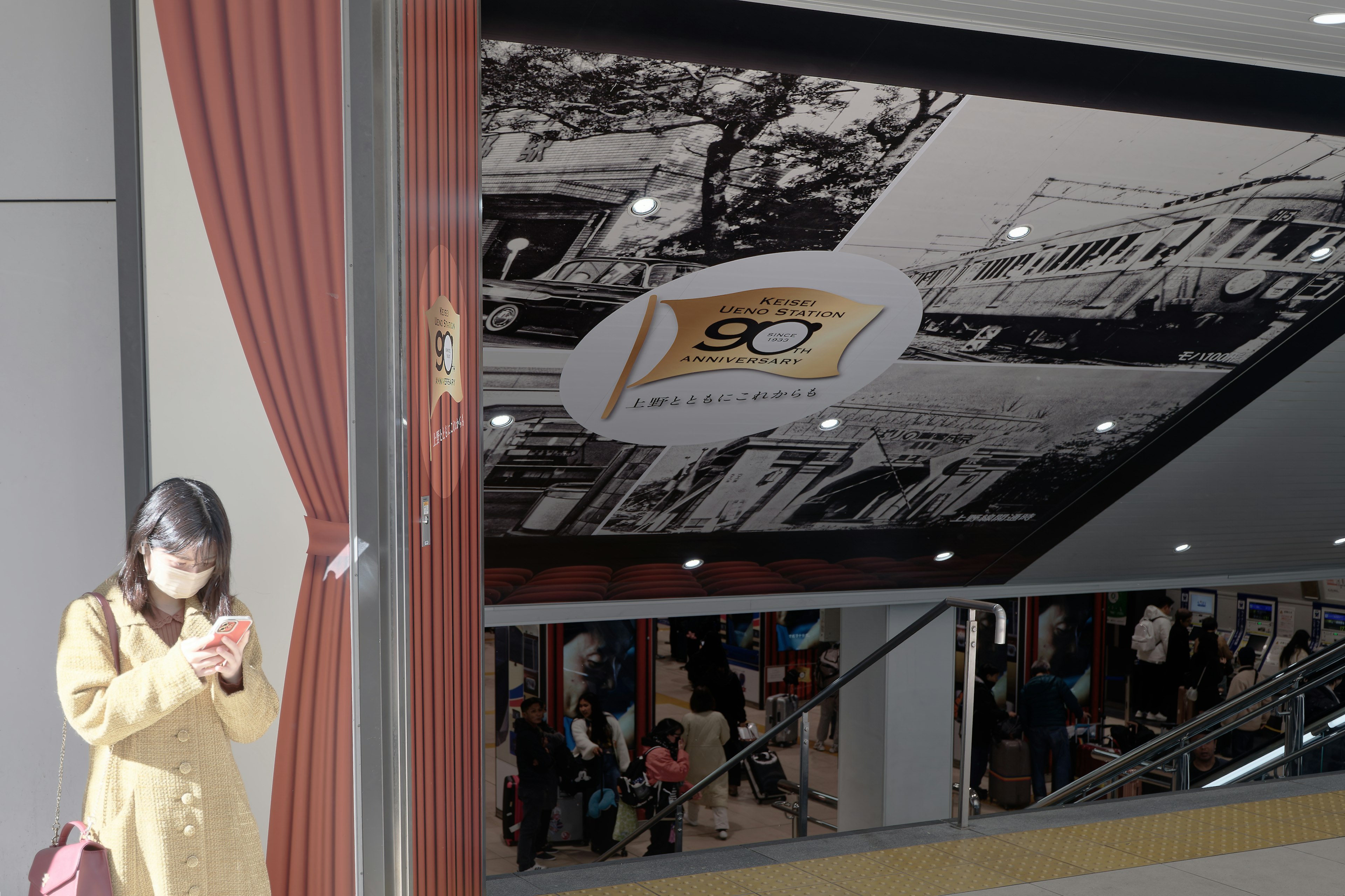 Intérieur d'un centre commercial avec une femme en manteau jaune et une œuvre d'art au plafond en noir et blanc