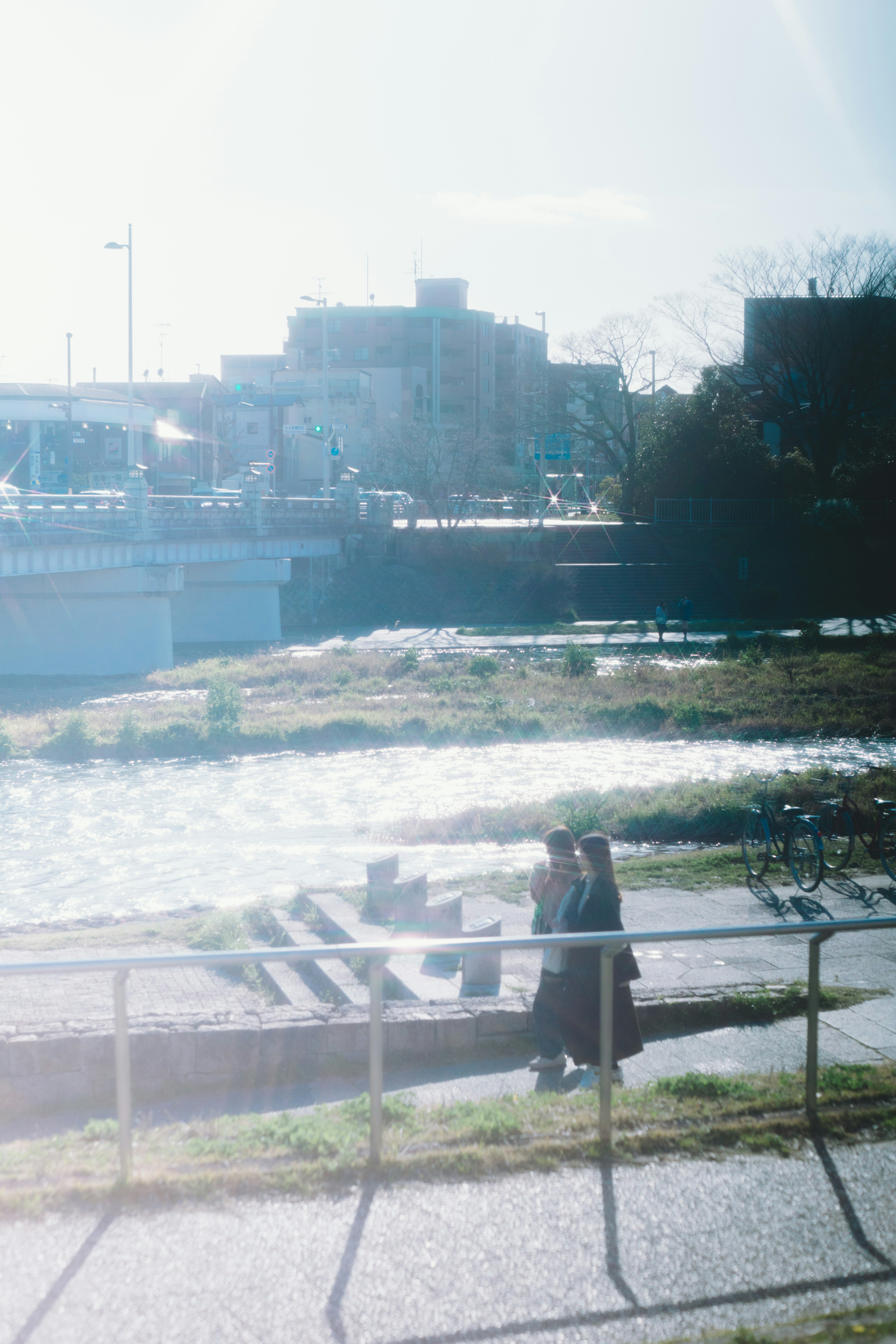 Silhouettes of people walking along a riverside pathway with a cityscape in the background