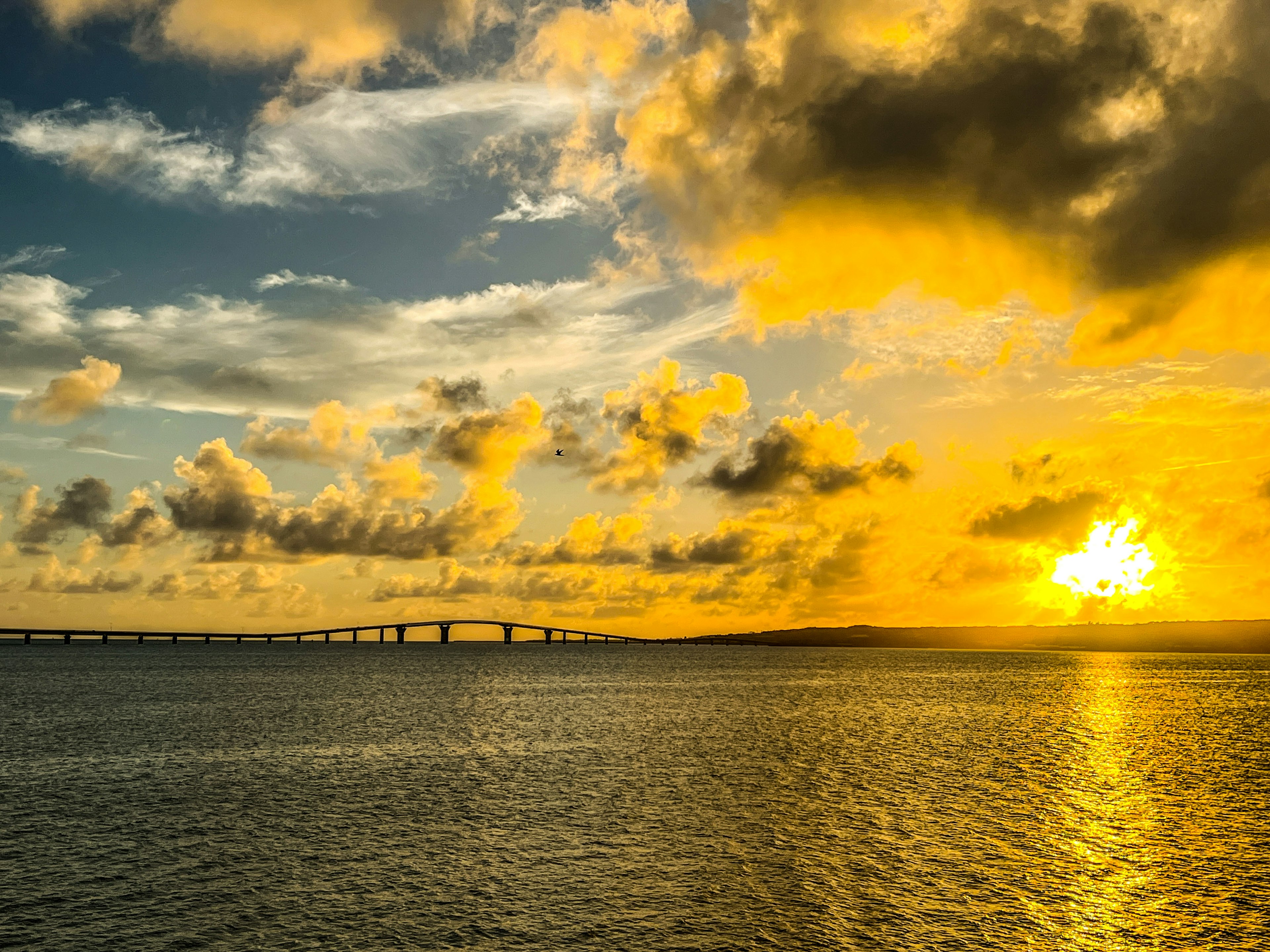 Pemandangan matahari terbenam yang indah di atas lautan dengan jembatan dan awan di langit