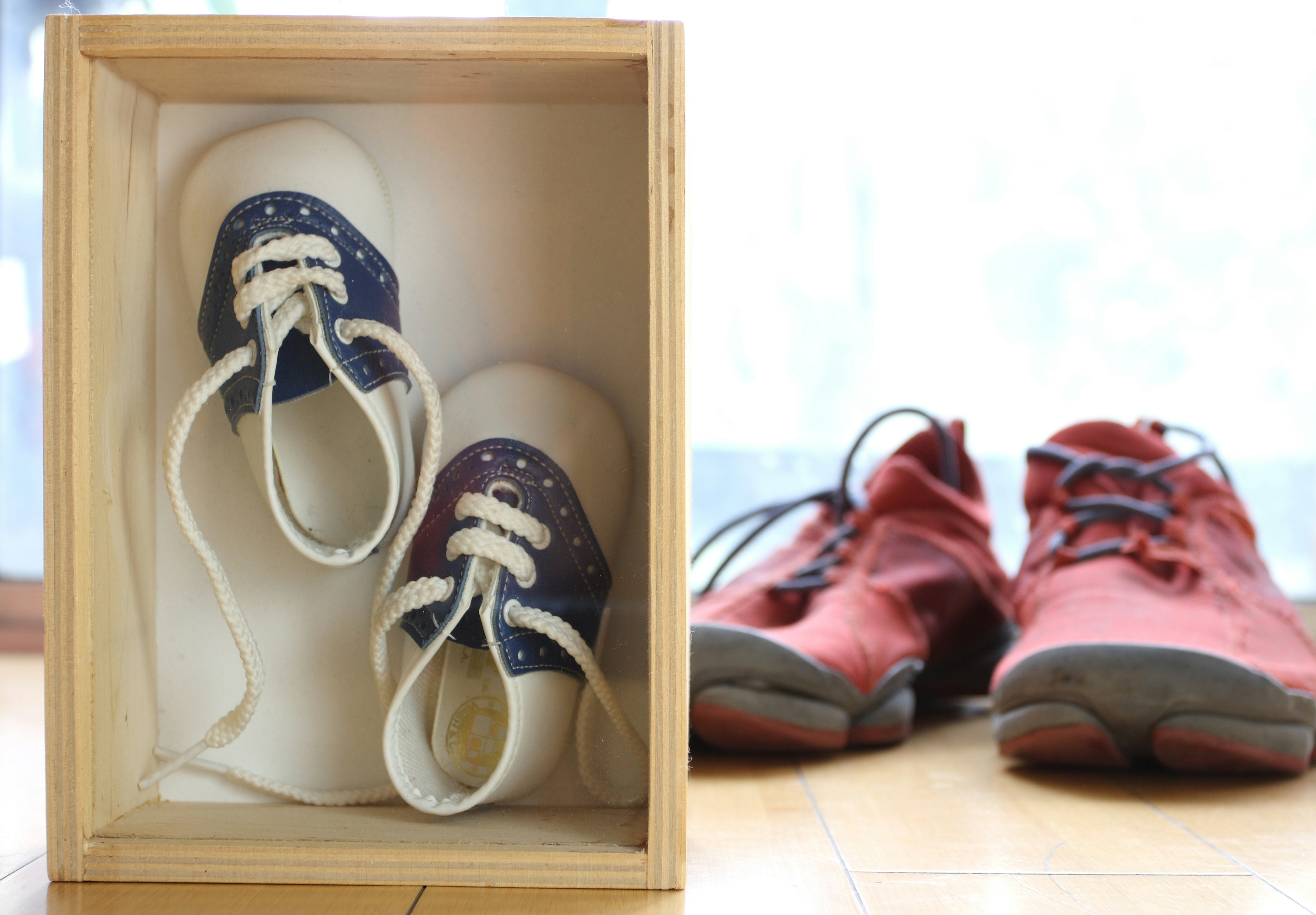 Petites chaussures dans une boîte en bois à côté de chaussures rouges