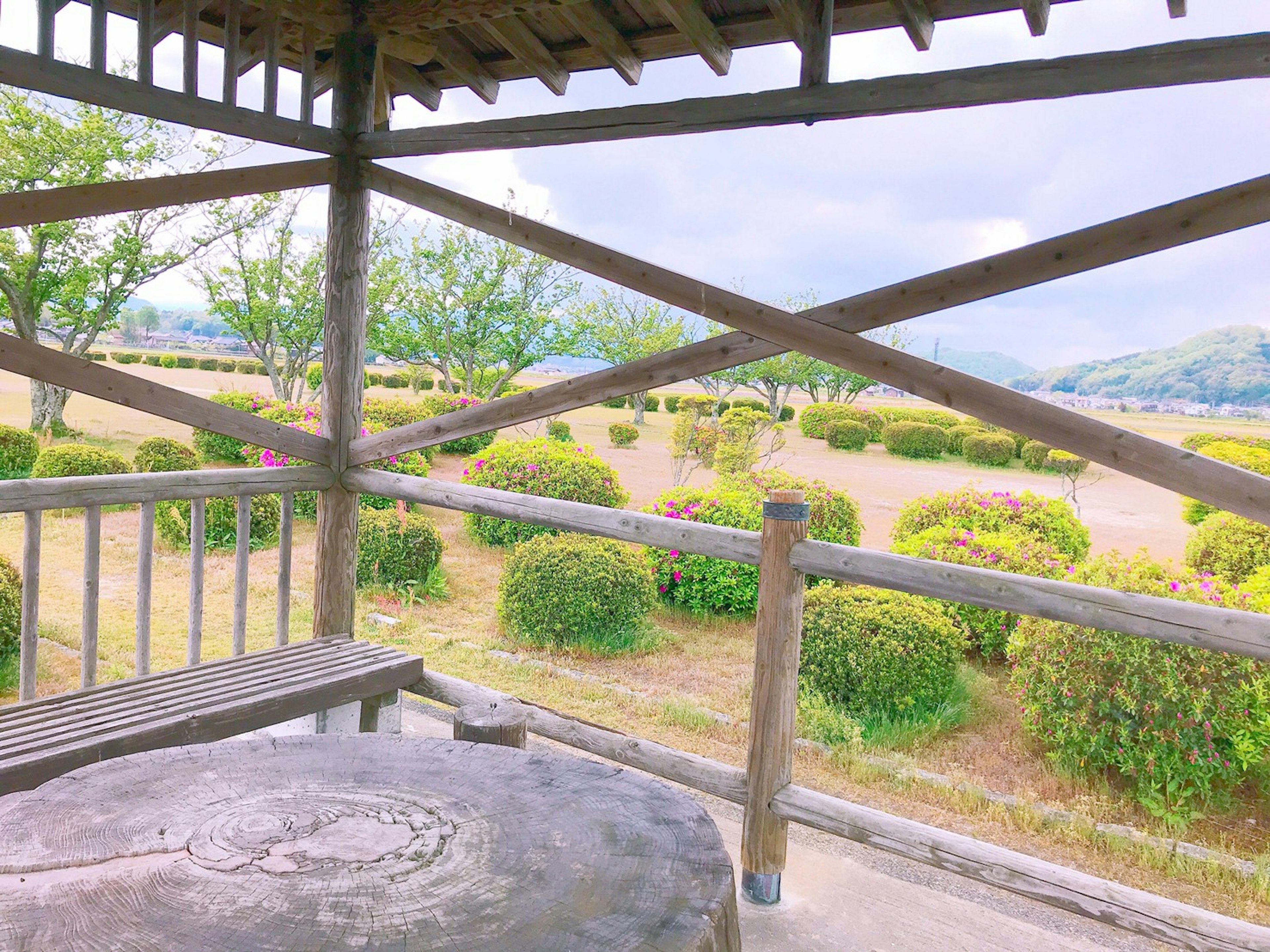 Pemandangan indah dari gazebo kayu dengan semak-semak hijau dan langit yang tenang