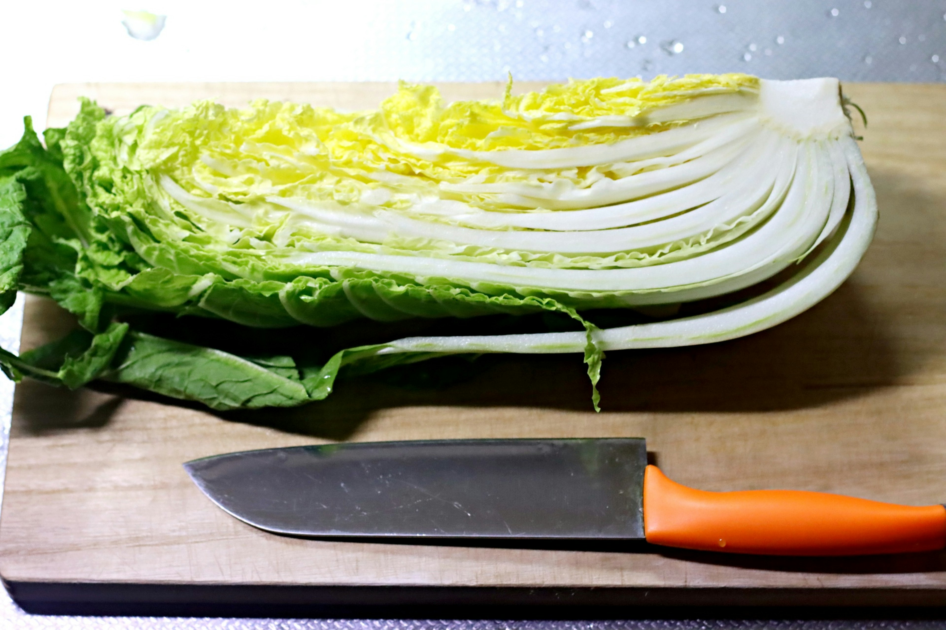 Sliced napa cabbage with an orange knife on a wooden cutting board