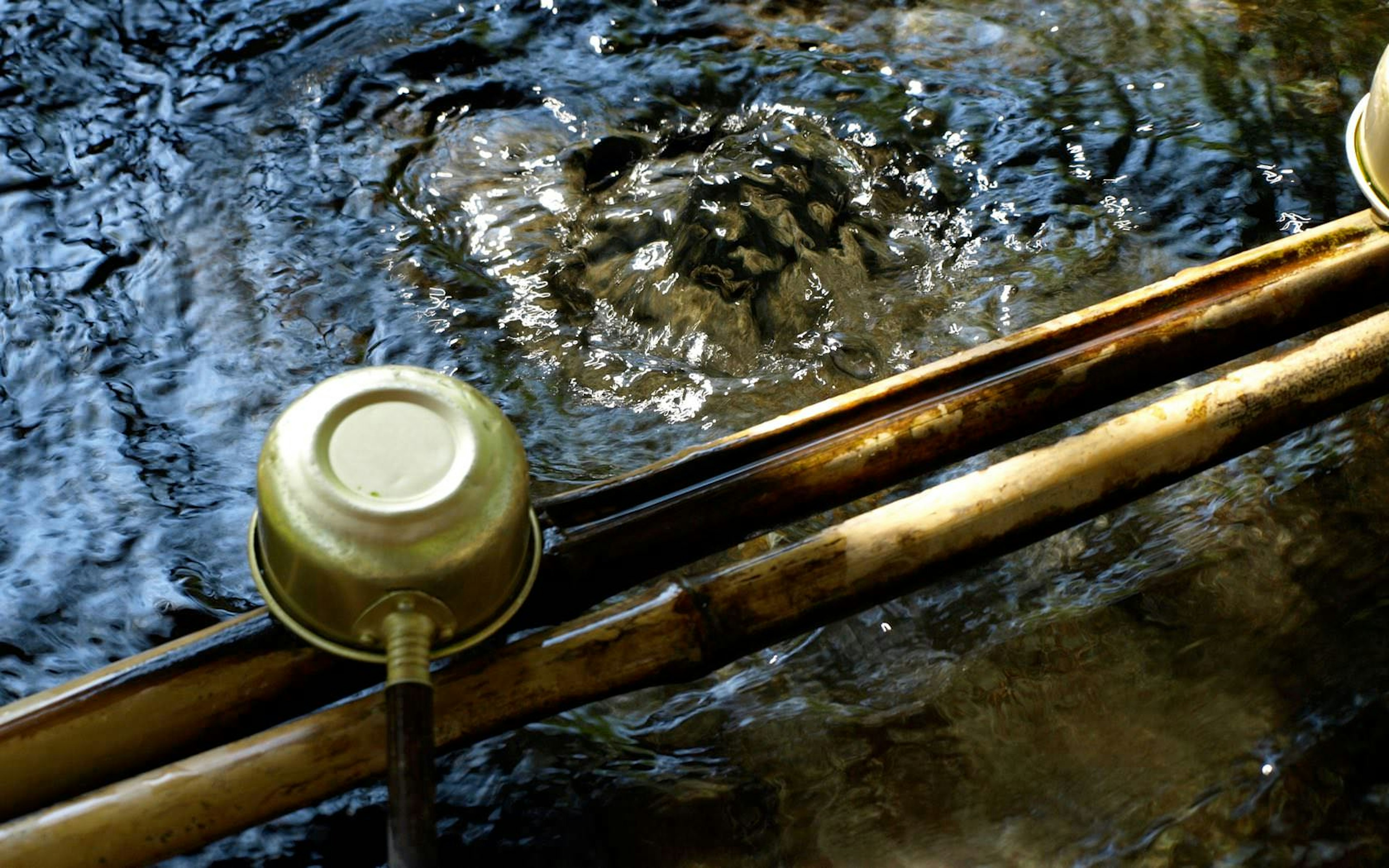 Scene near a clear stream featuring a metal bowl and bamboo stick above the water surface