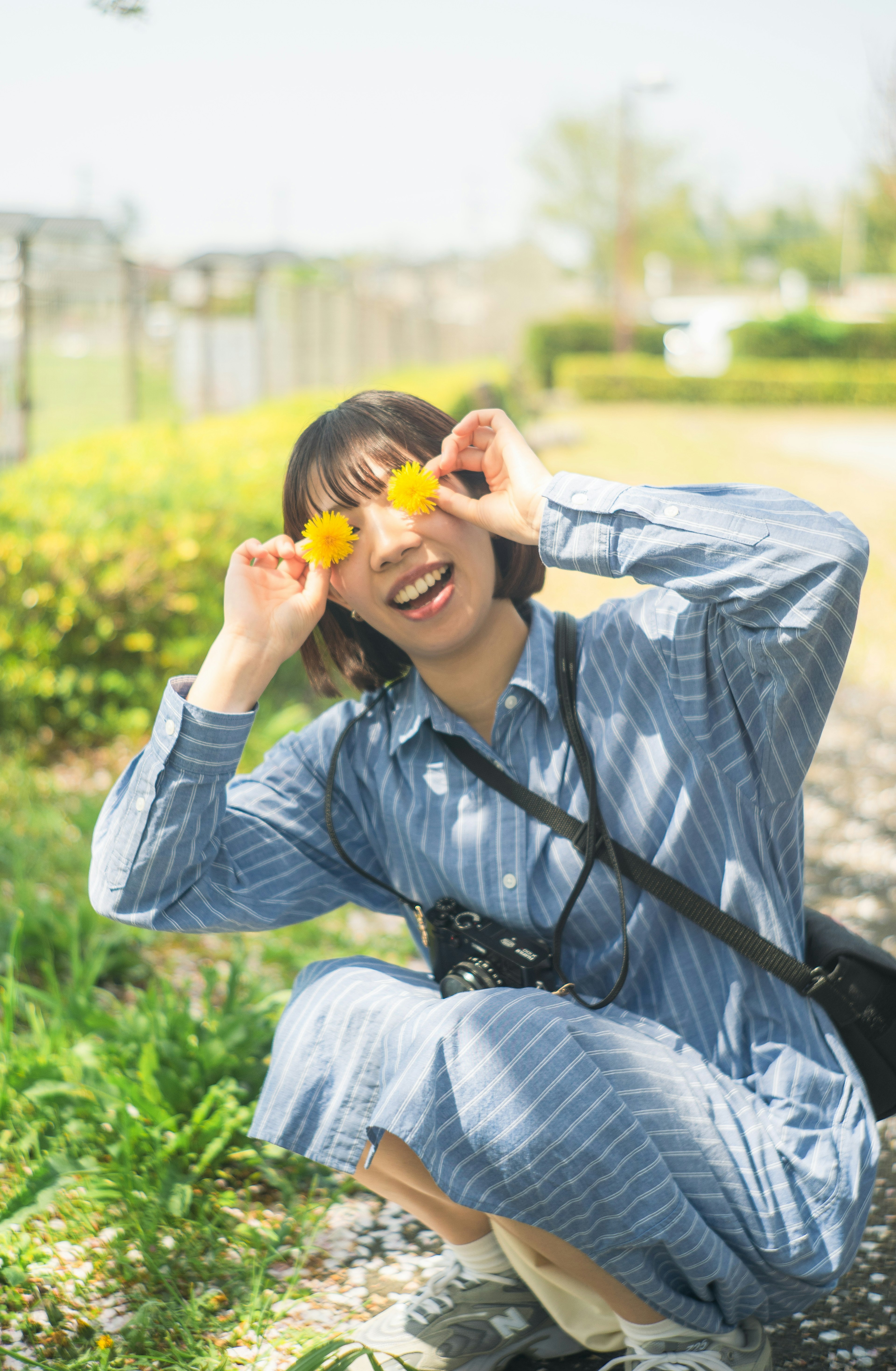 青いストライプのドレスを着た女性がオレンジ色の花を持って笑顔でポーズをとっている