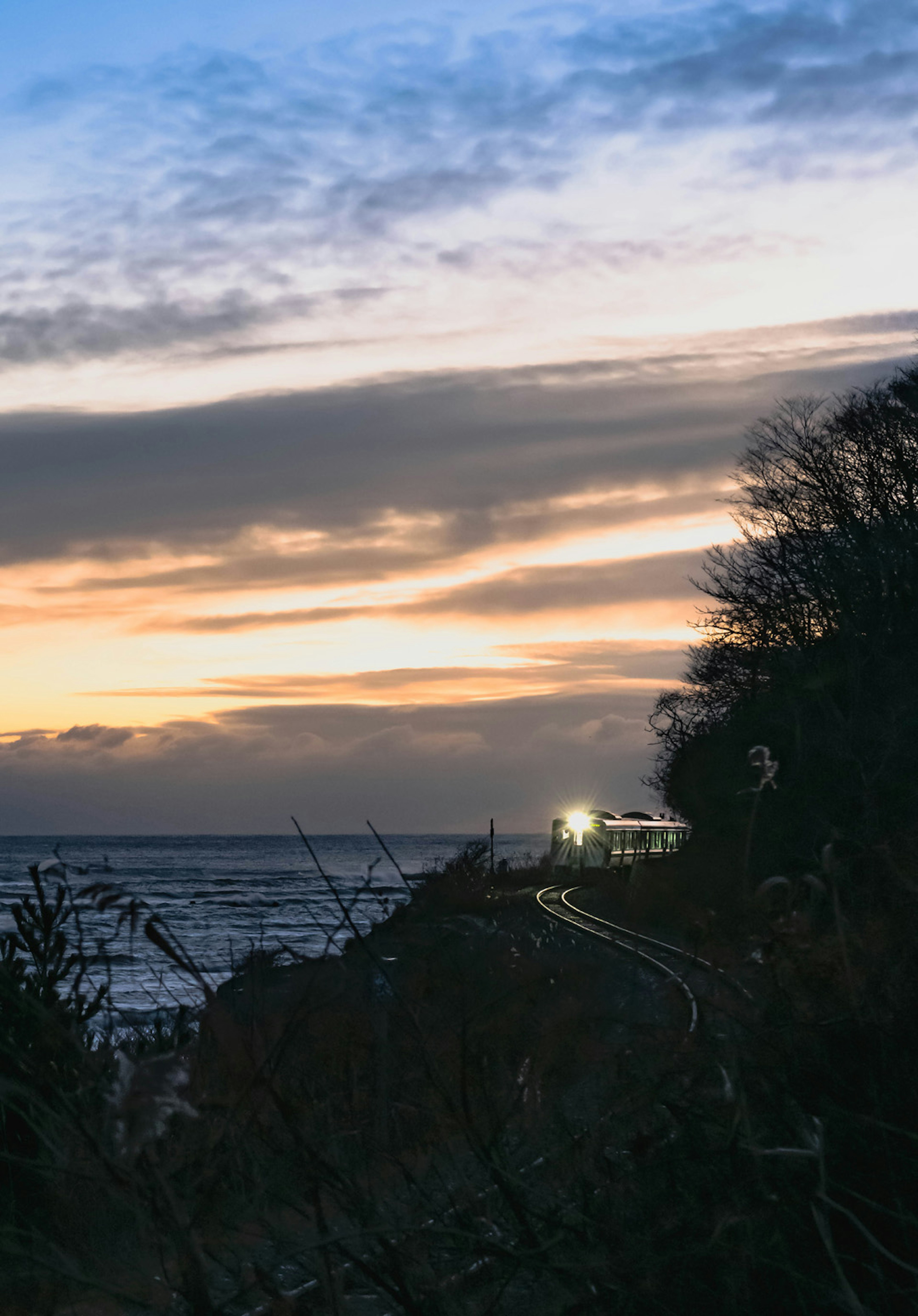 Voie ferrée le long de la côte au coucher du soleil avec une gare illuminée