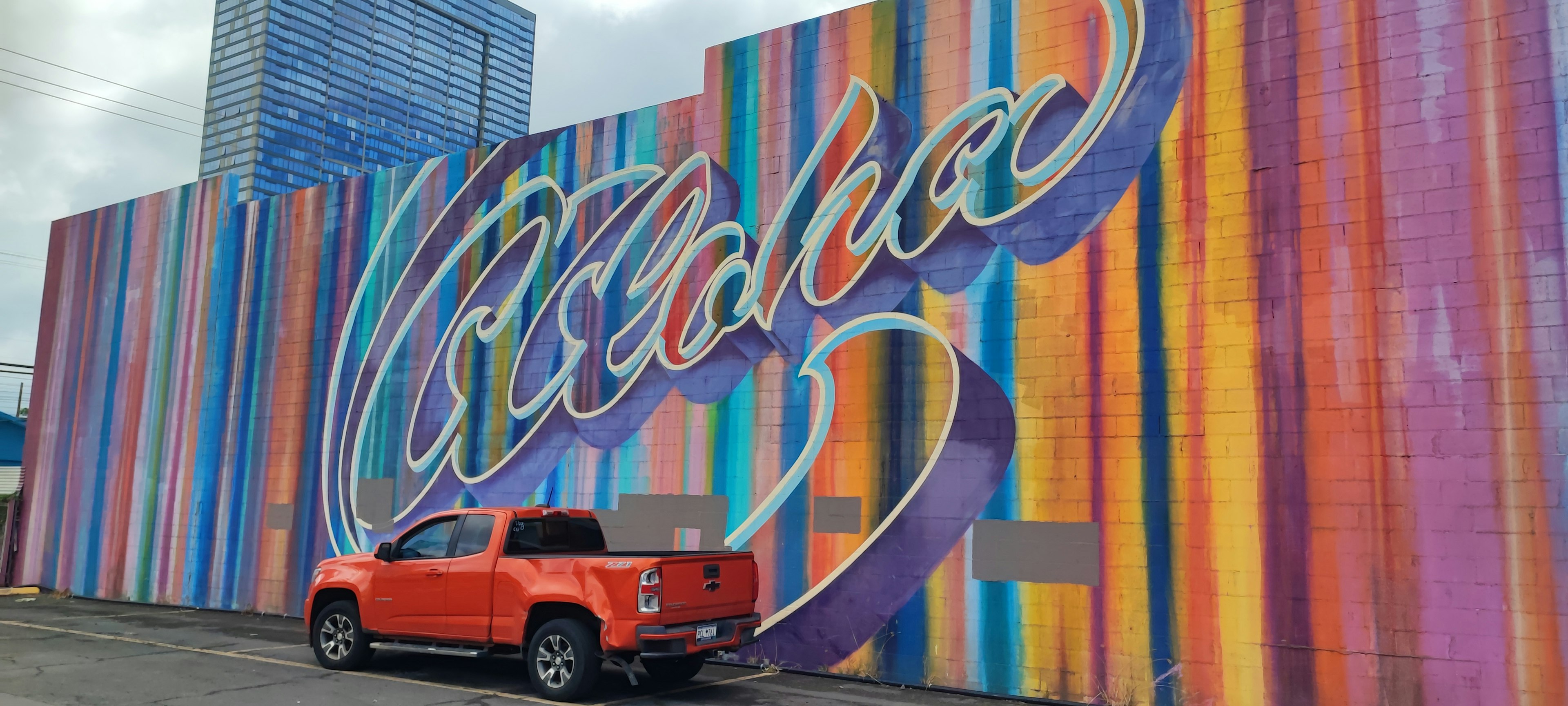 Dinding bergaris warna-warni dengan kata 'Aloha' dan truk merah