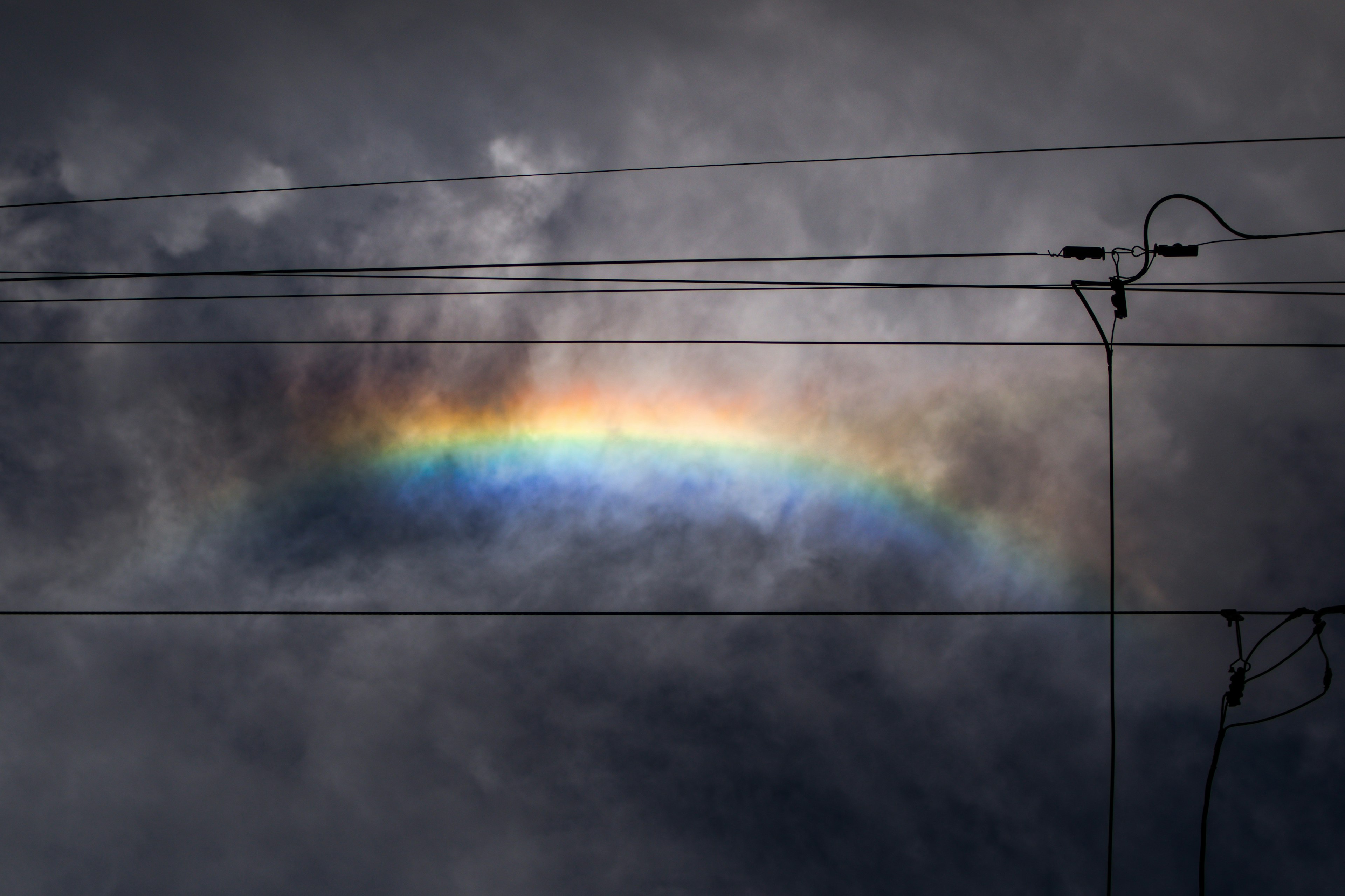 Regenbogen, der zwischen dunklen Wolken mit silhouettierten Stromleitungen erscheint