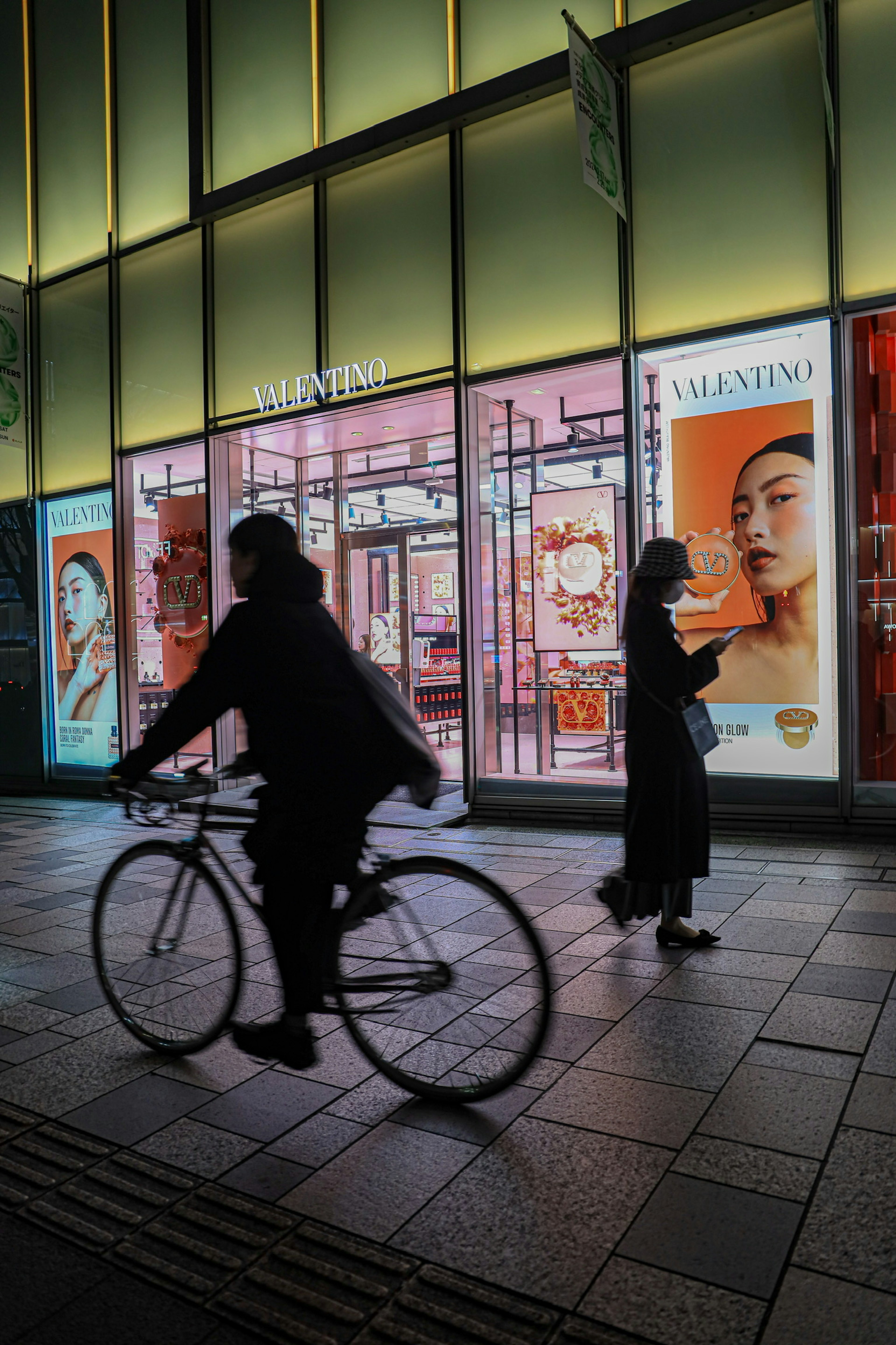 Silhouette di un ciclista e di una donna che cammina contro uno sfondo urbano vibrante di notte