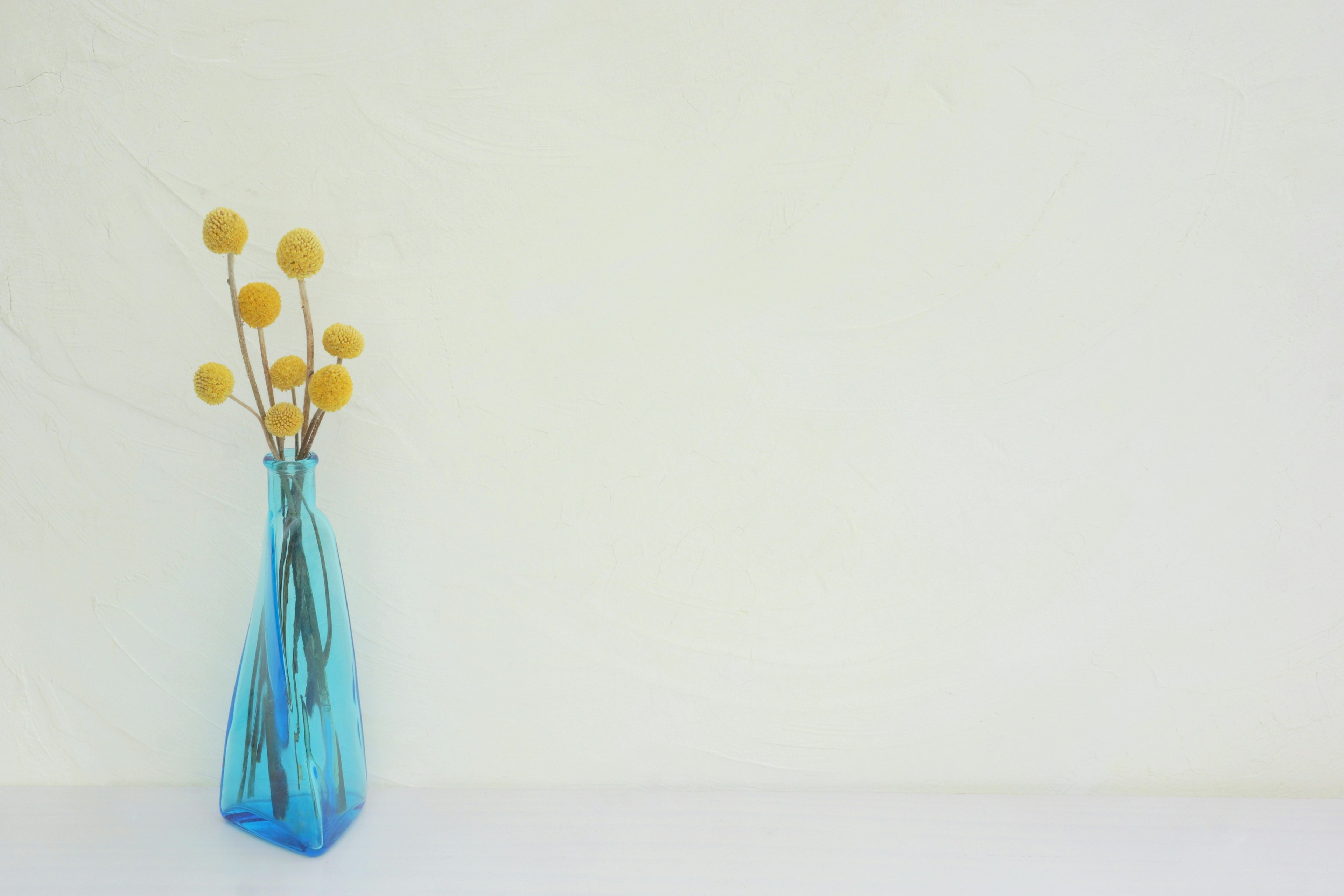 Un arrangement simple avec un vase en verre bleu et des fleurs jaunes