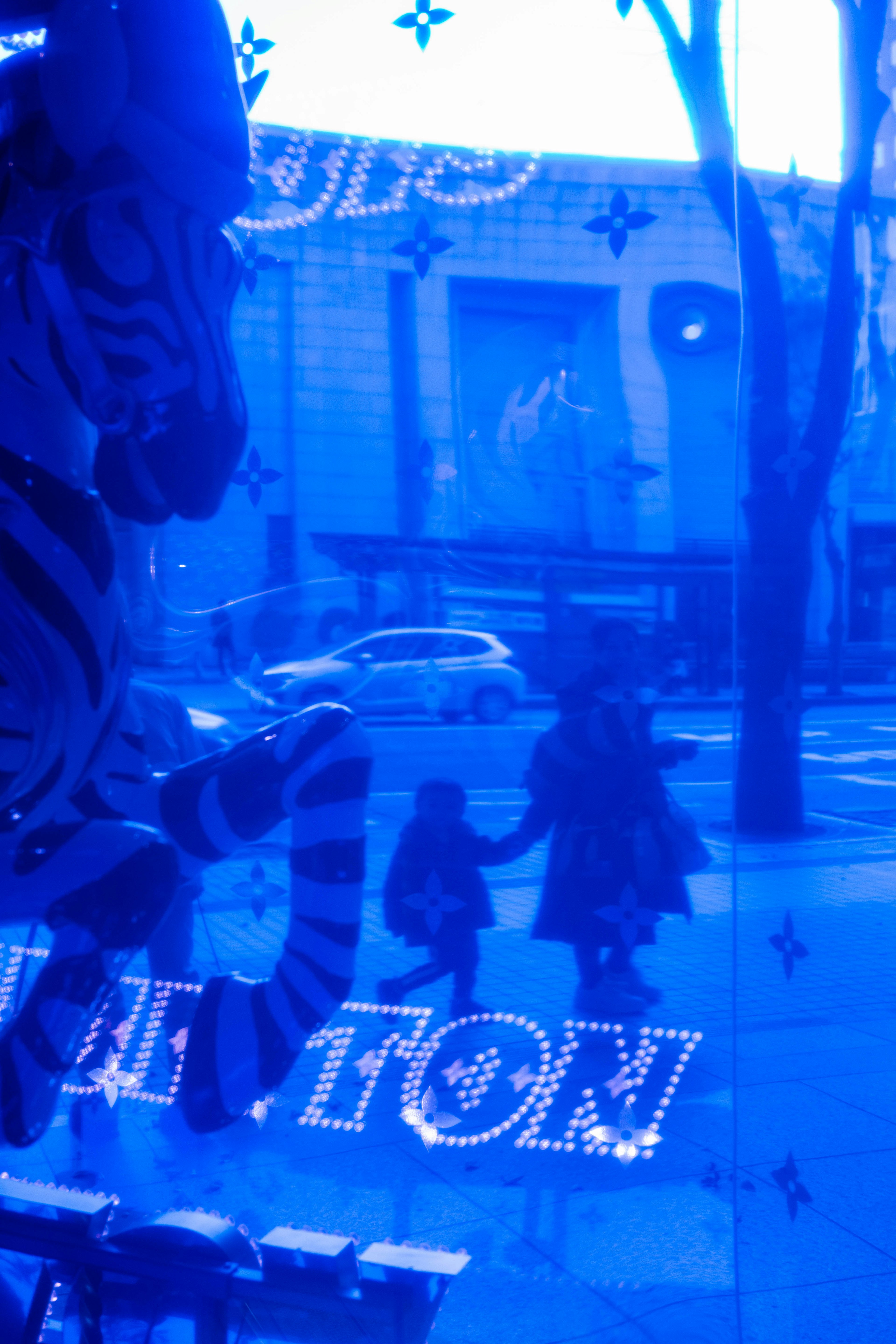 Blue tinted window display reflecting silhouettes of people and striped object