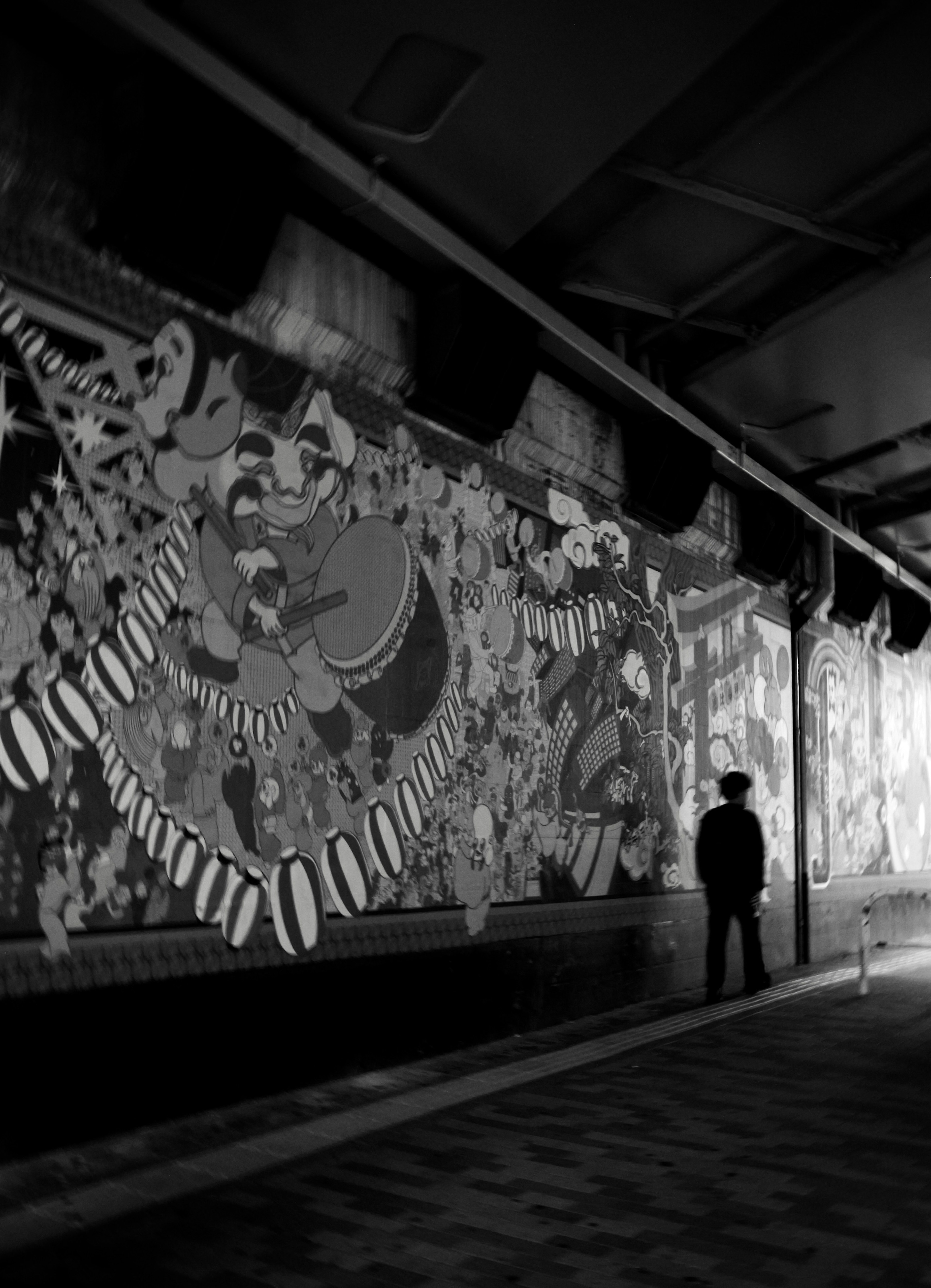 Silueta de una persona de pie en un pasillo con murales en blanco y negro