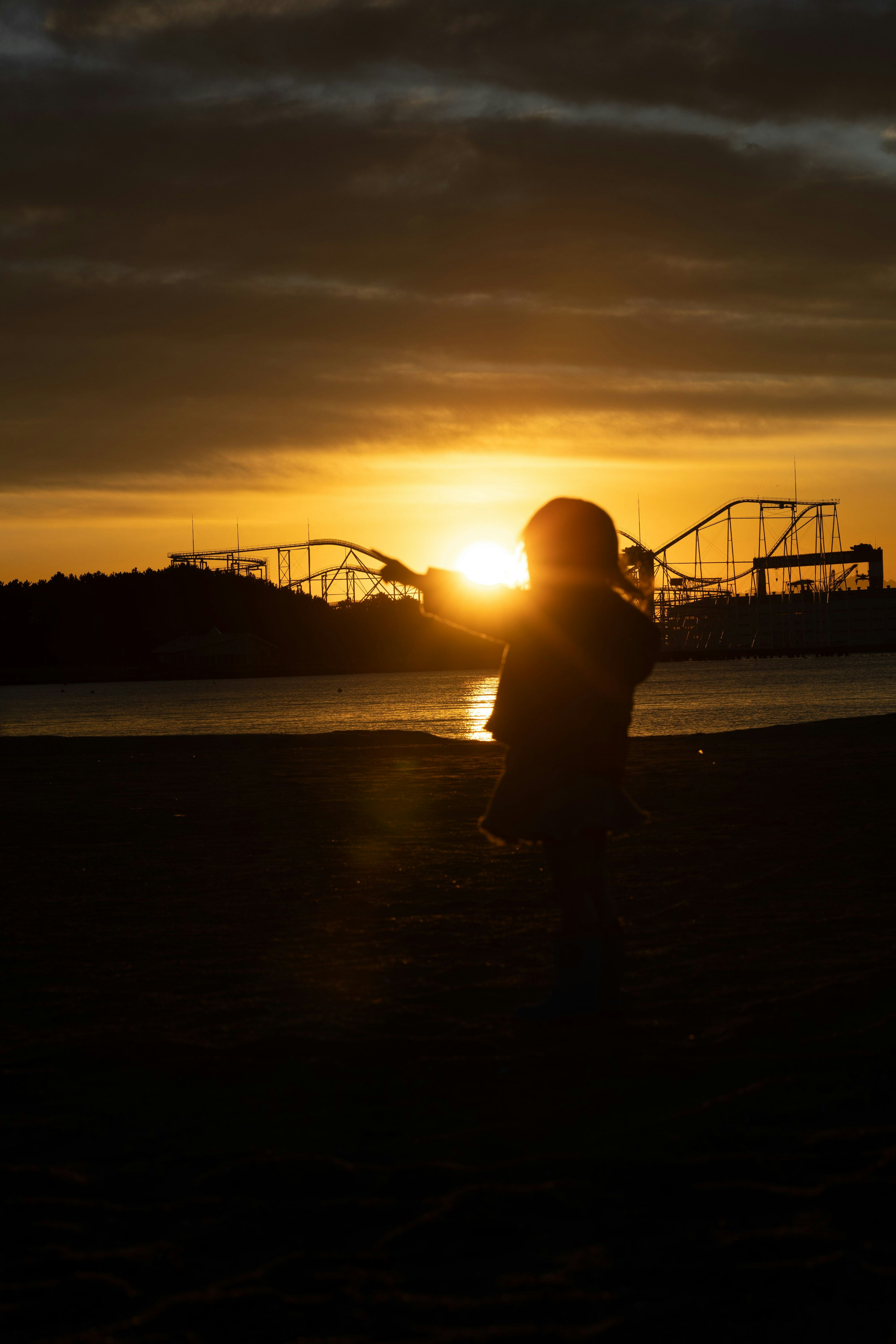 Silhouette d'une personne au coucher du soleil avec des montagnes russes de parc d'attractions en arrière-plan