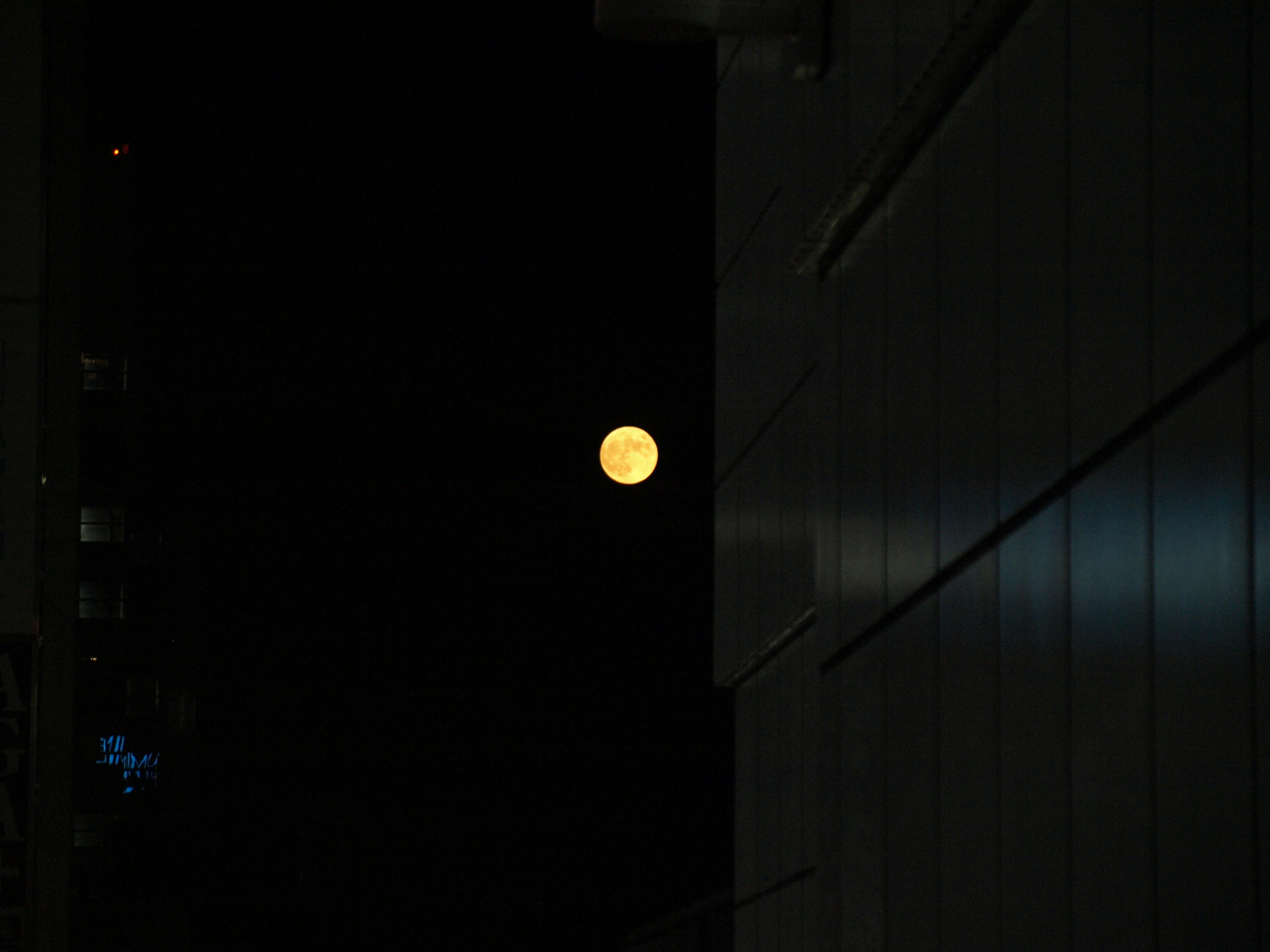 Luna brillante en el cielo nocturno junto a un edificio oscuro