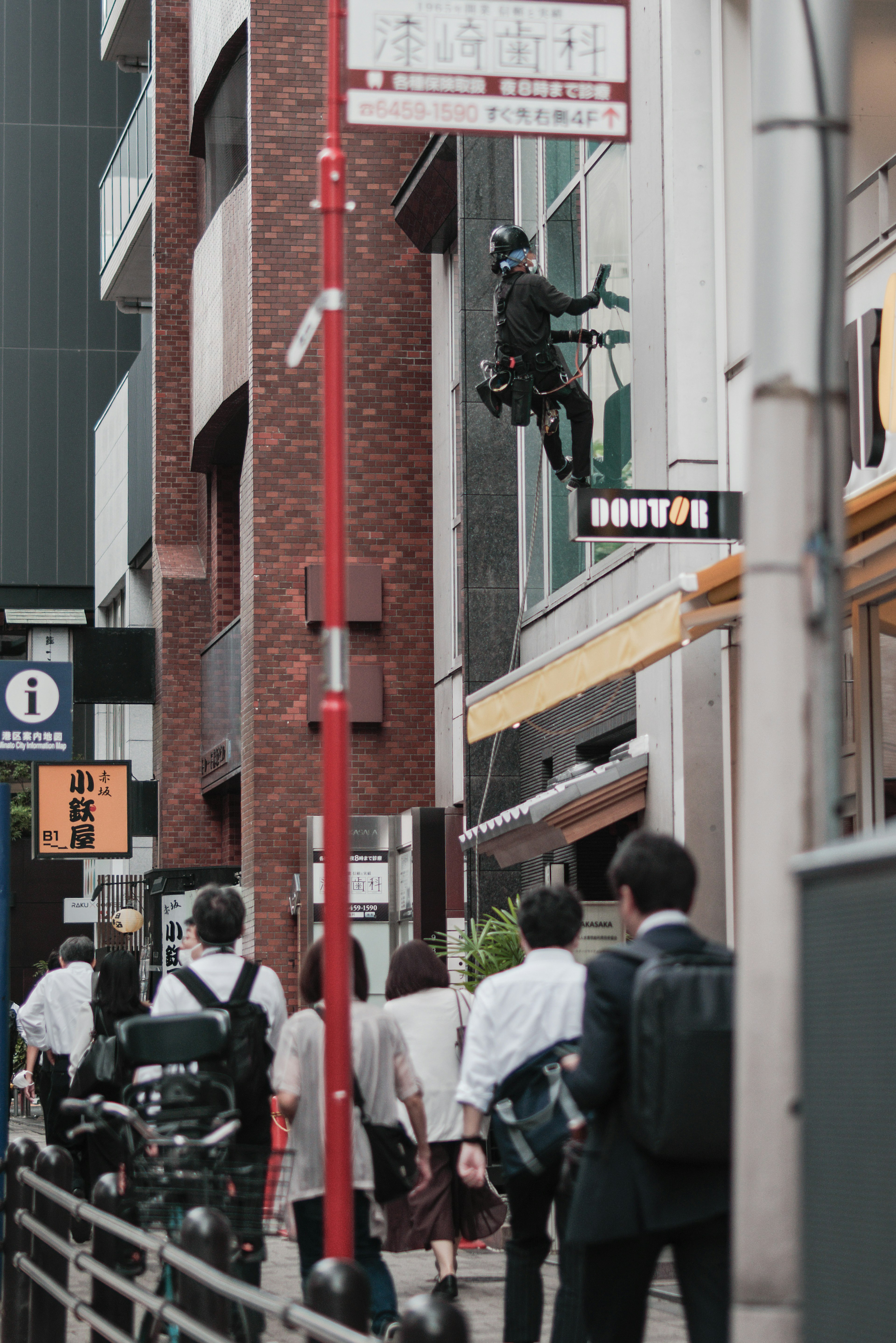 Worker climbing a building wall with pedestrians nearby