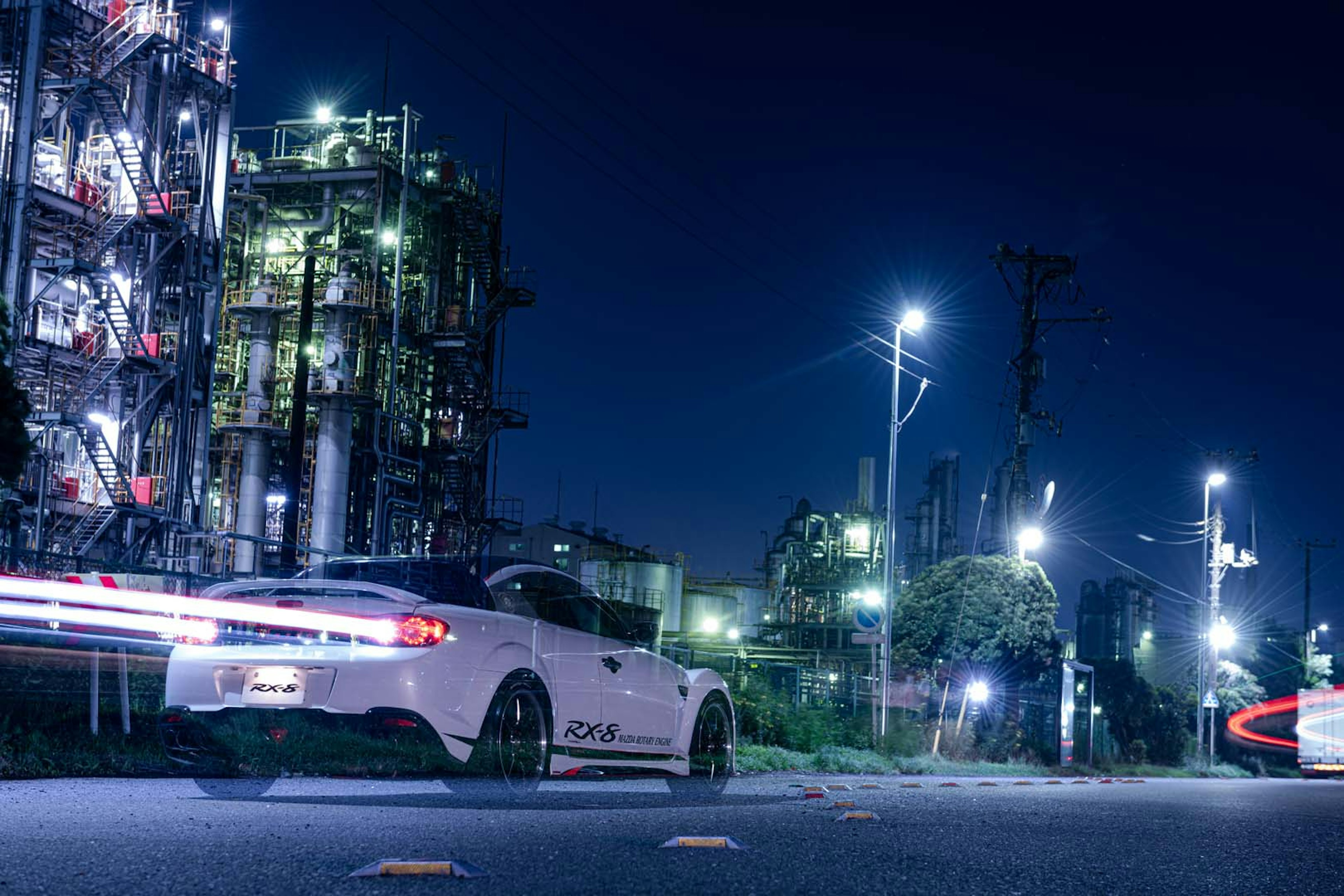 Coche deportivo blanco conduciendo en un área industrial de noche con fondo de fábrica