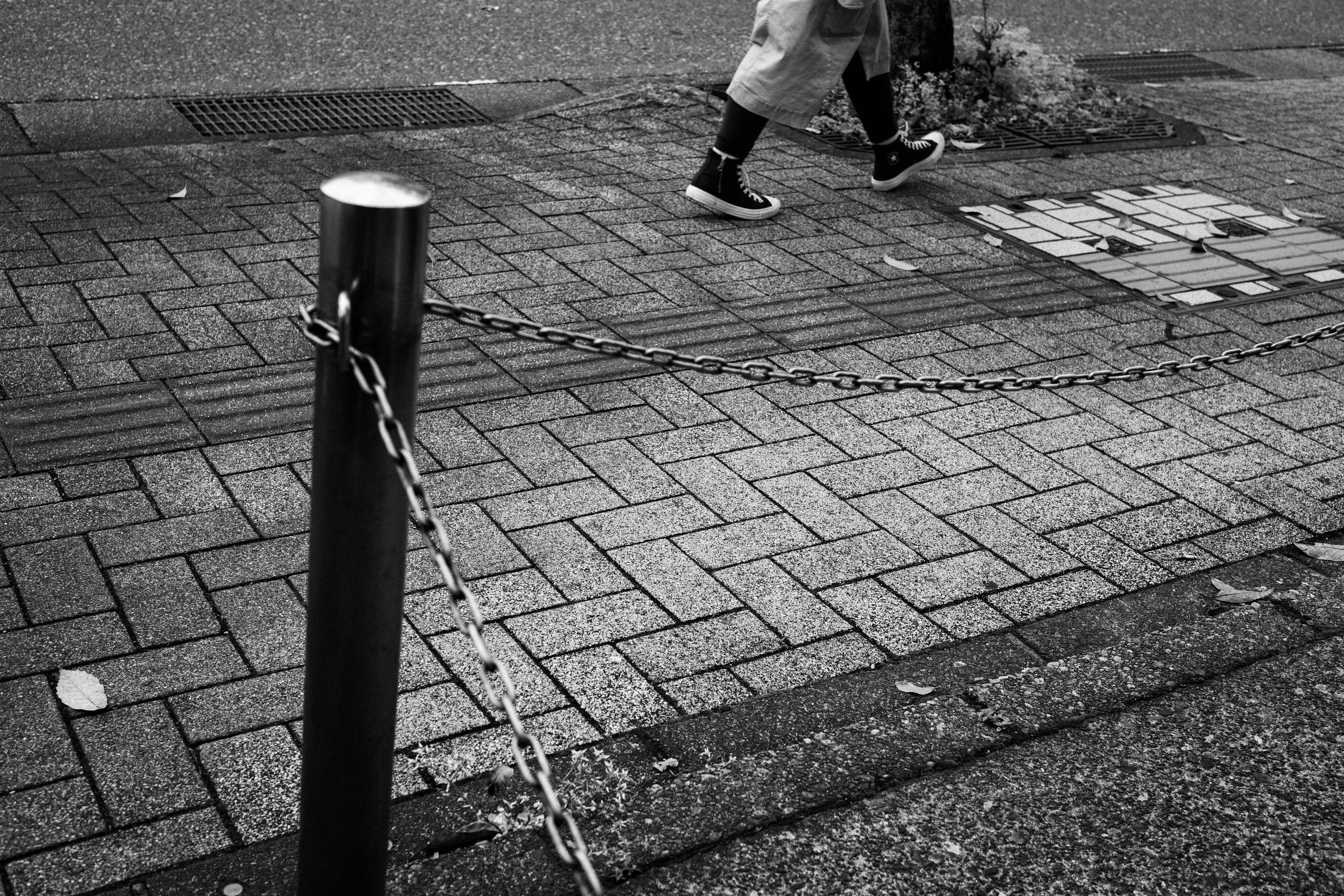 Eine Person, die in einer schwarz-weißen Stadtlandschaft mit einem angeketteten Pfosten geht