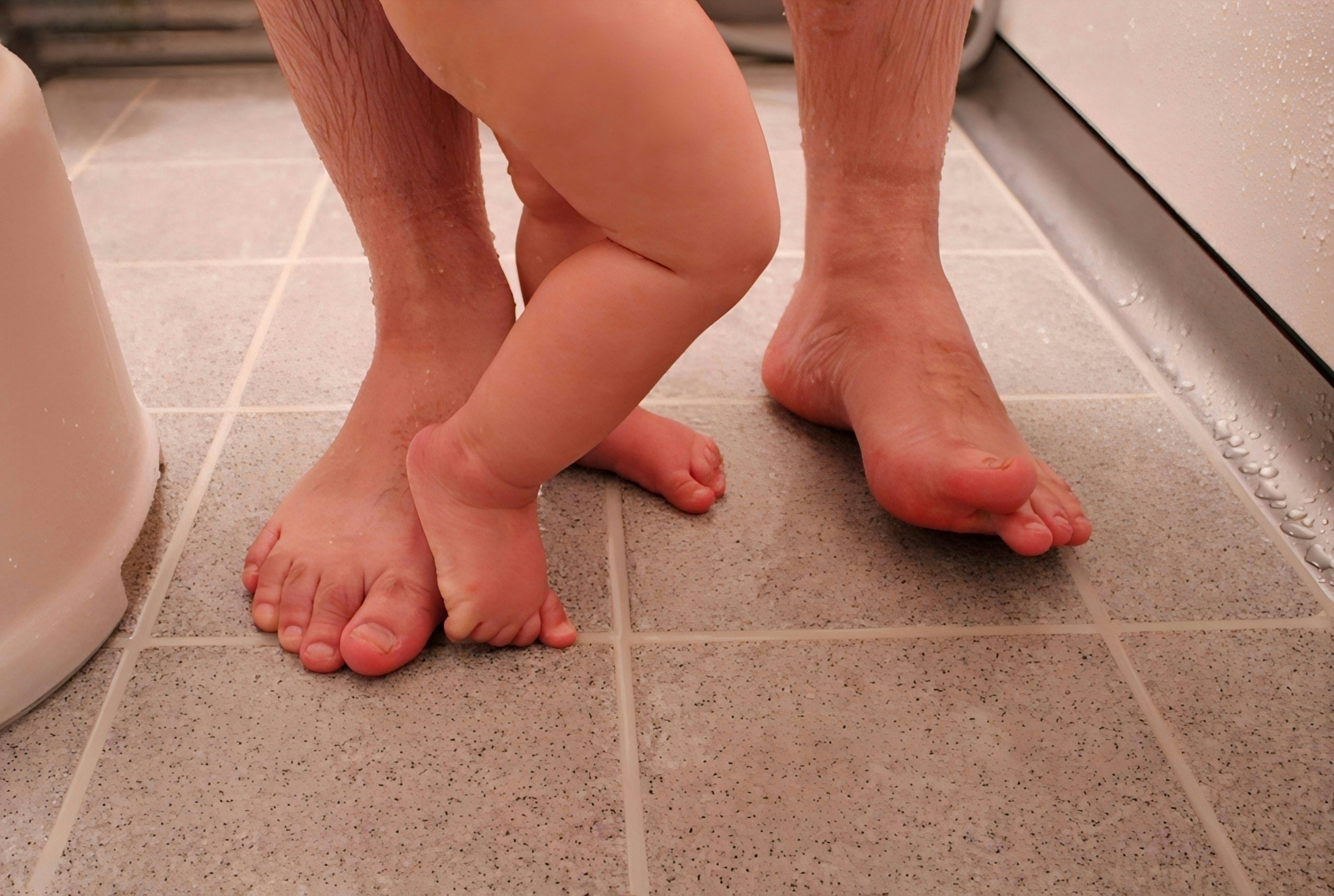 Foto dei piedi di un bambino e di un adulto su un pavimento di bagno