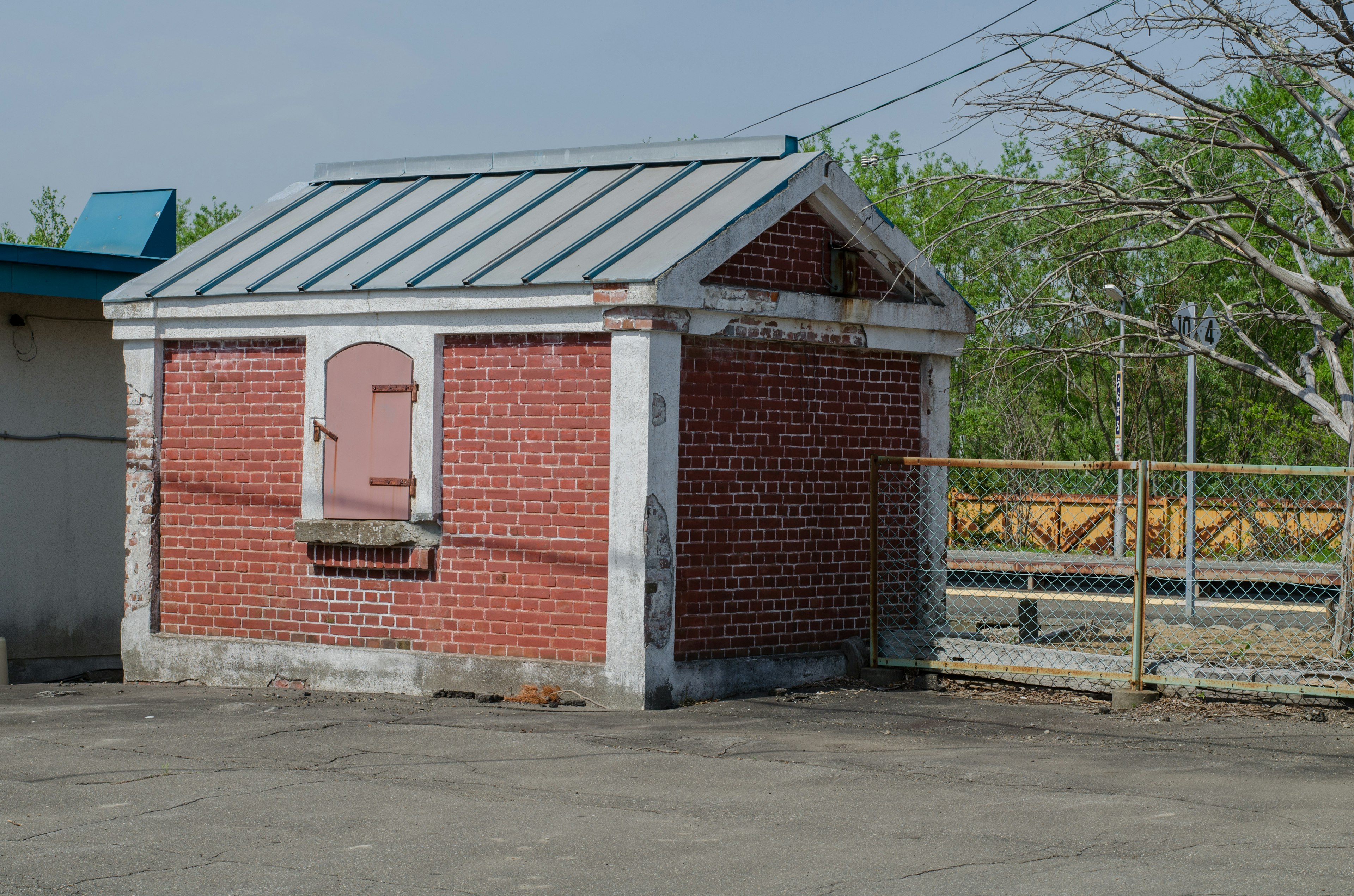 Red brick shed with a metal roof surrounded by a fence