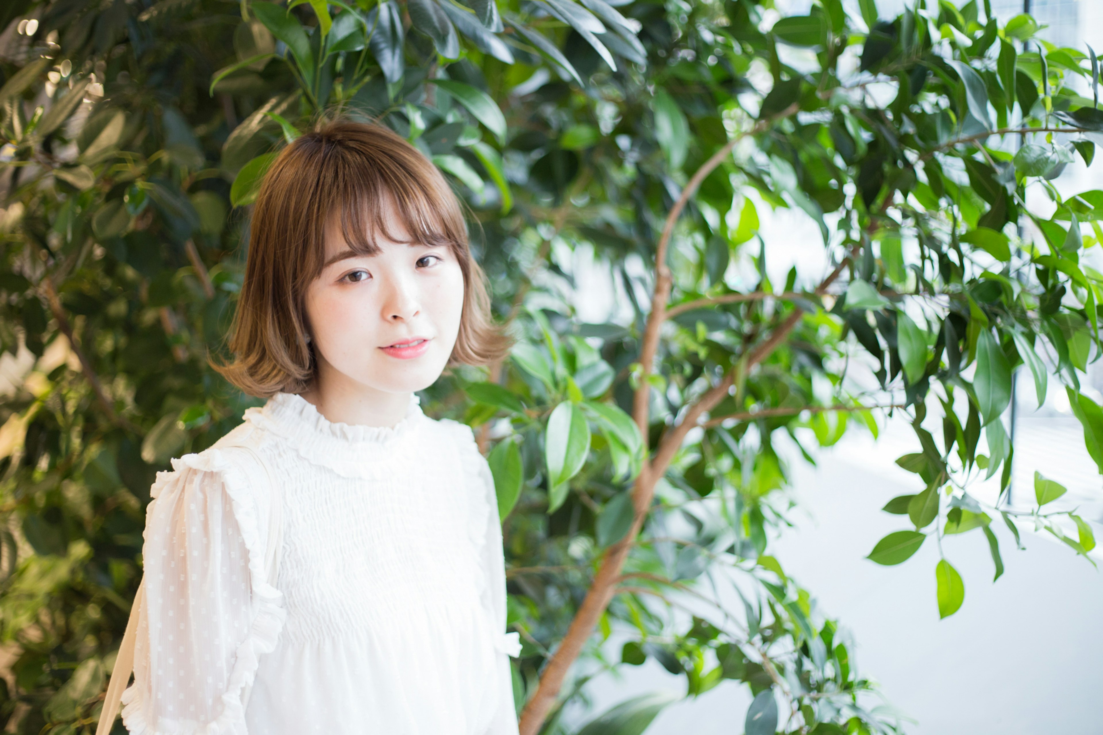 Portrait of a young woman standing in front of green plants wearing a white dress