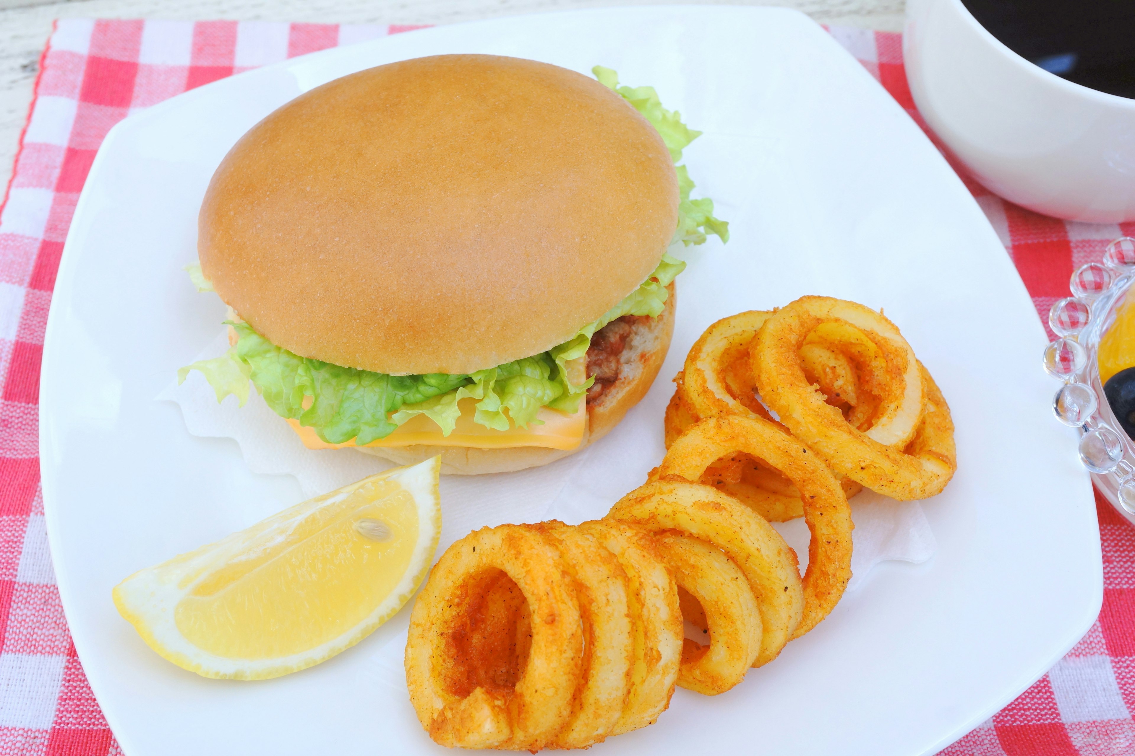 Una hamburguesa con lechuga y papas fritas en espiral servida en un plato blanco con una rodaja de limón