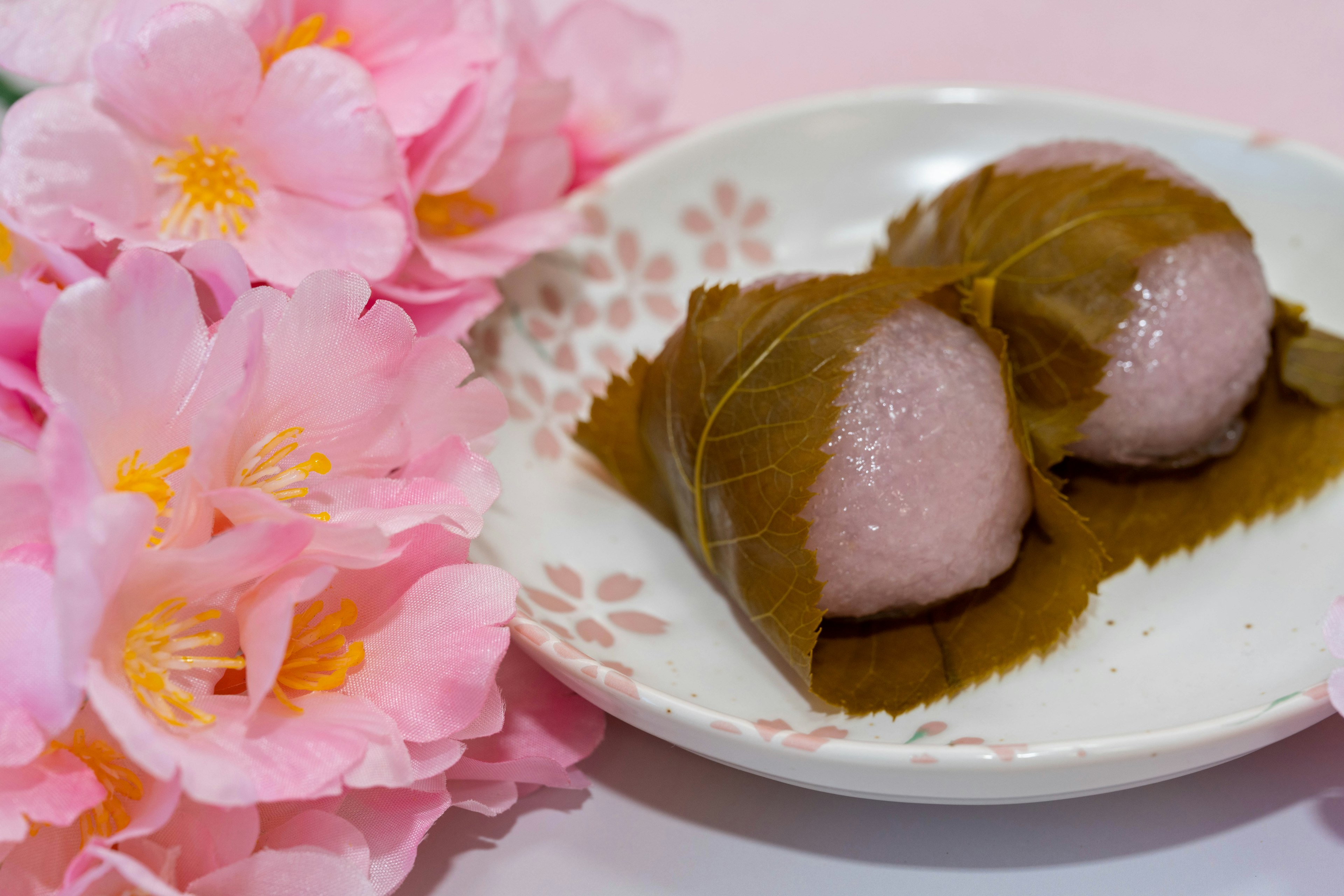 Dolce di riso giapponese avvolto in foglie servito con fiori di ciliegio rosa