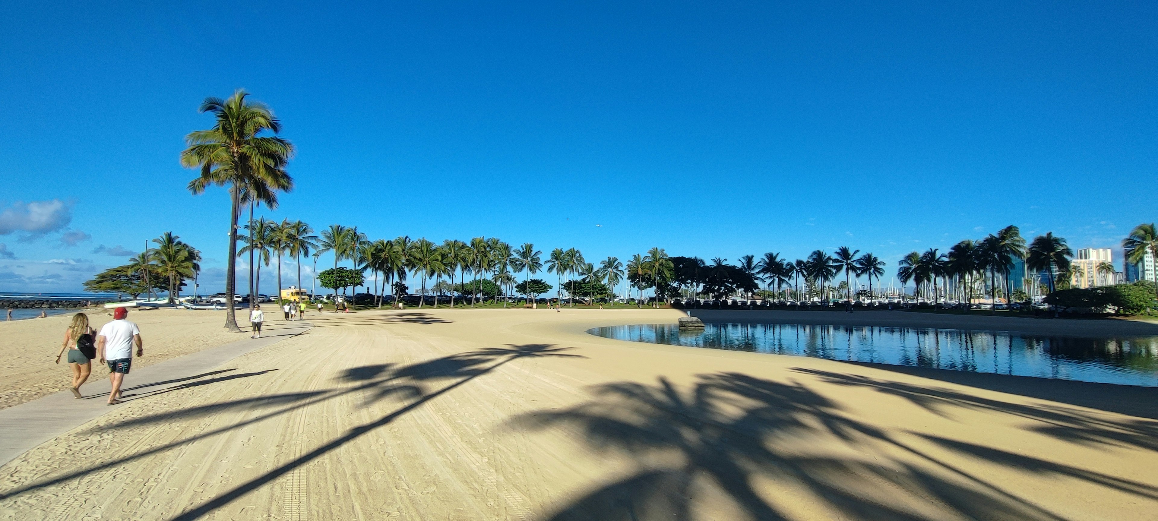 Scène de plage avec des personnes marchant sous un ciel bleu et des ombres de palmiers