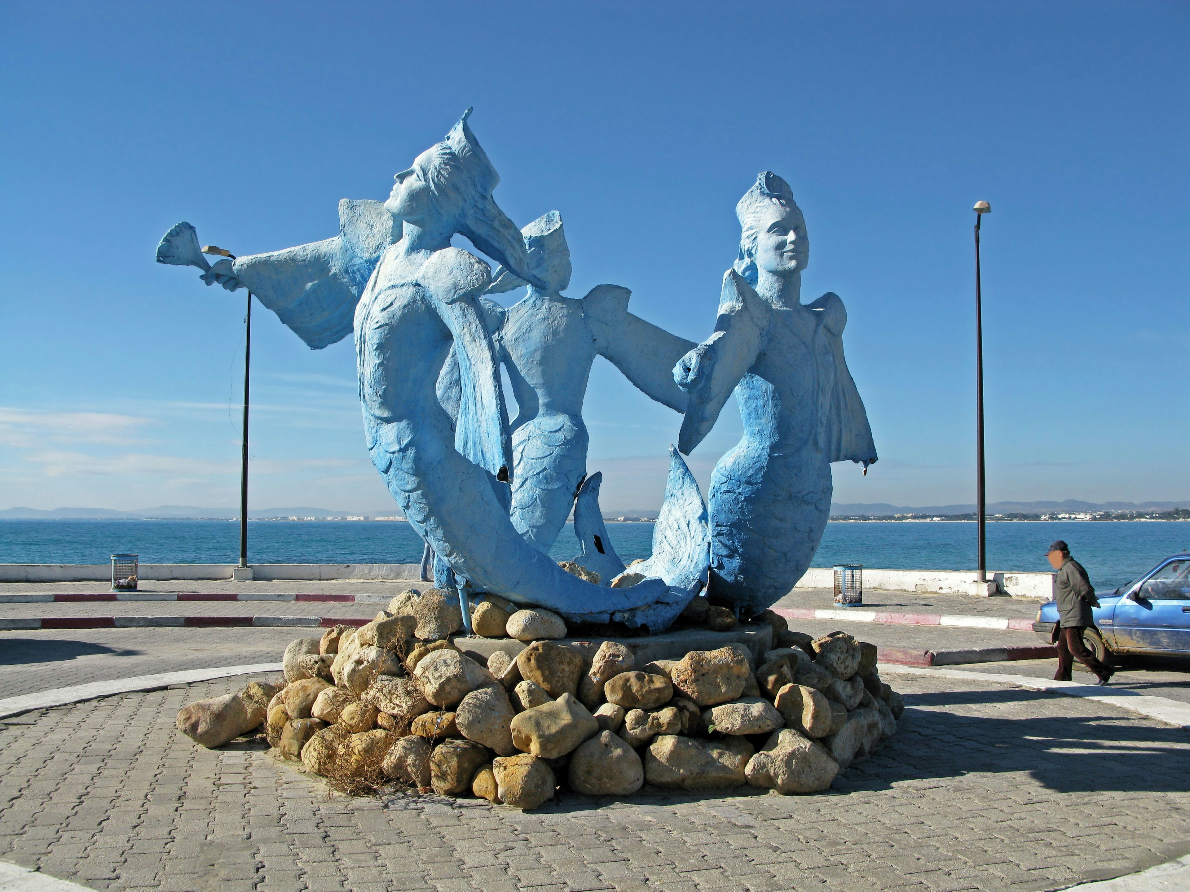 Scultura di sirena blu che si erge su rocce al mare