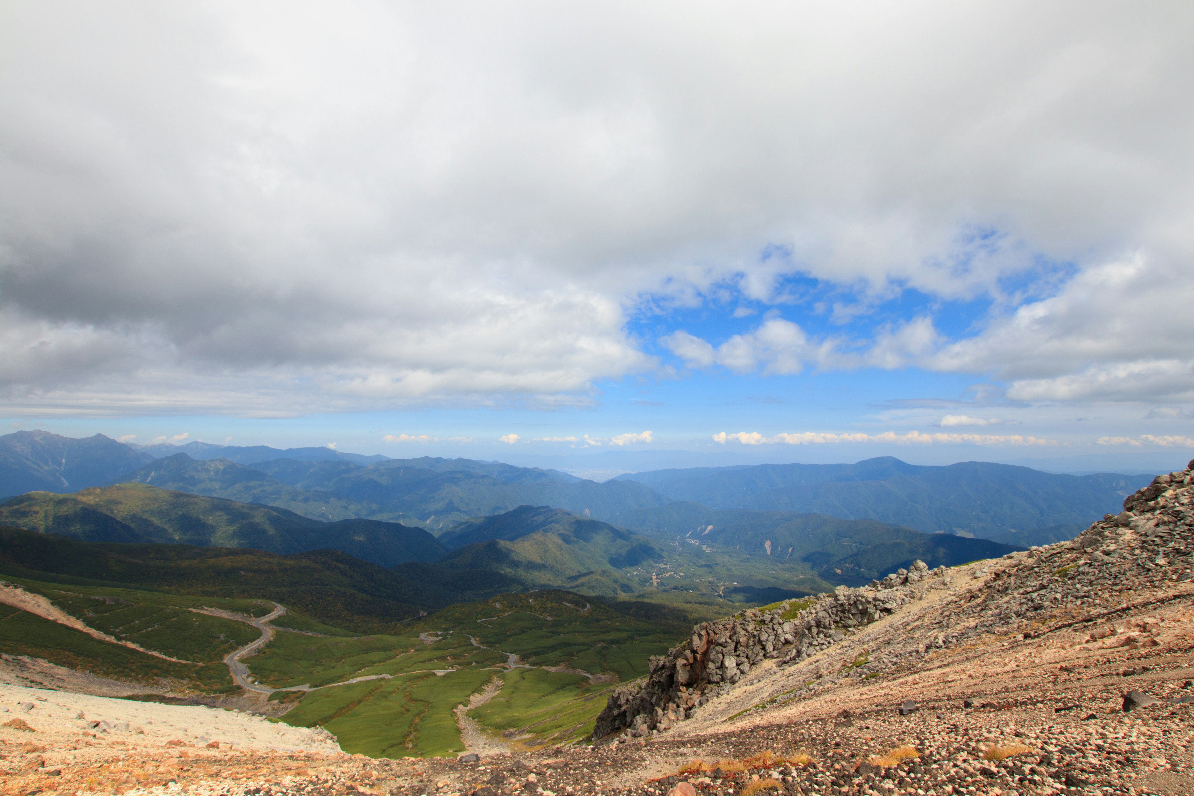 Pemandangan luas dari puncak gunung dengan bukit hijau dan langit berawan