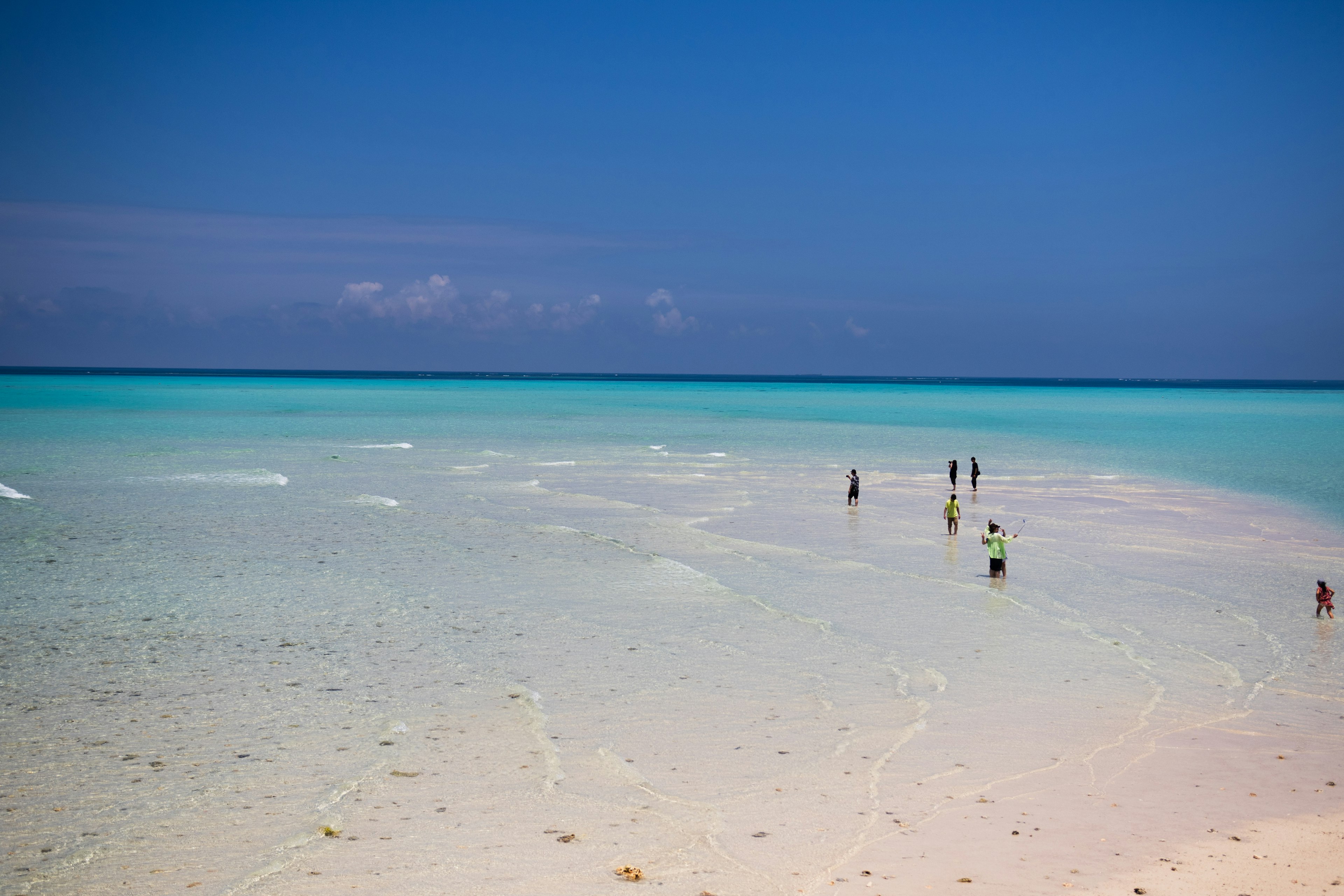 ผู้คนเพลิดเพลินกับทะเลสีฟ้าอ่อนตื้นๆ พร้อมชายหาดทรายขาว