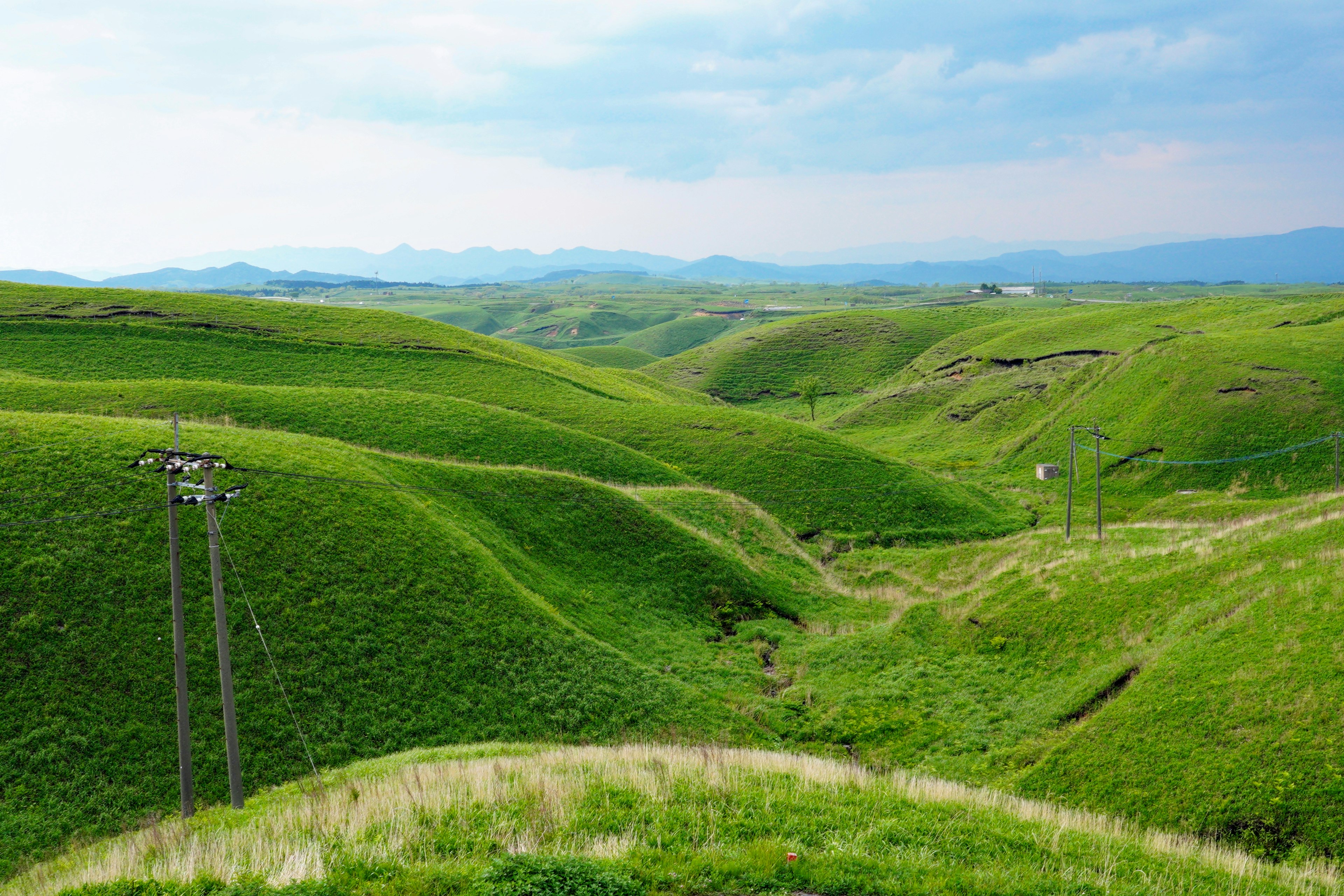 Collines verdoyantes sous un ciel bleu avec des poteaux électriques éparpillés