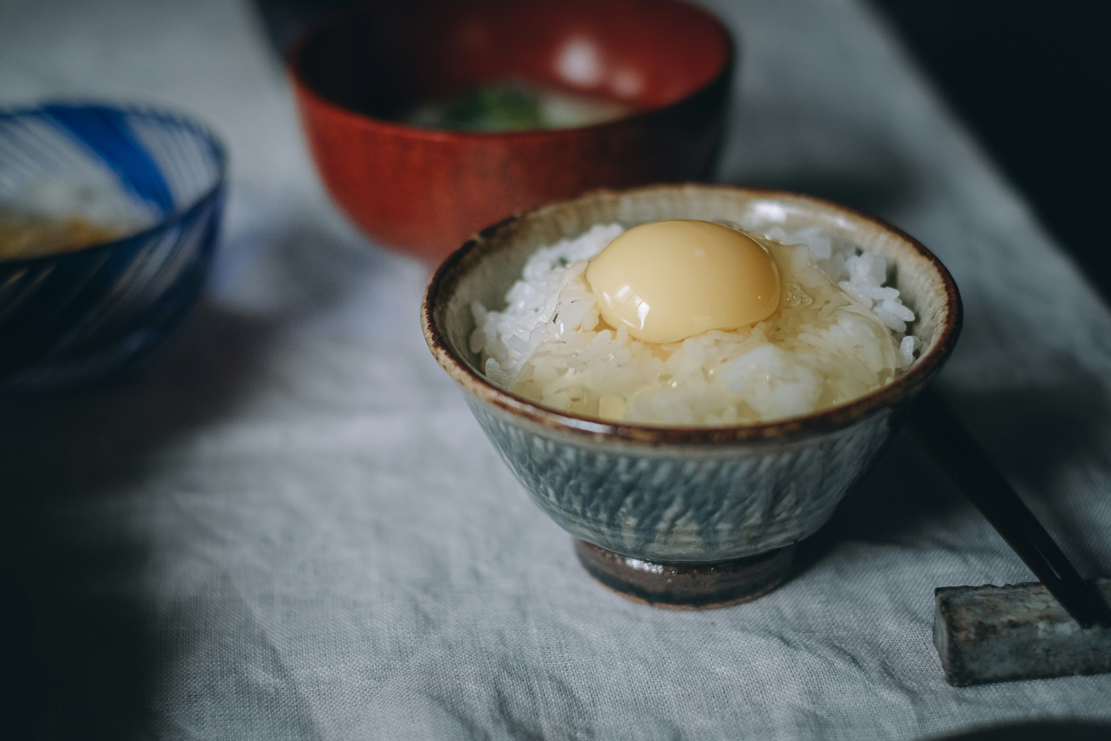 밥 위에 노른자가 있는 그릇과 배경에 빨간 그릇이 있는 식탁