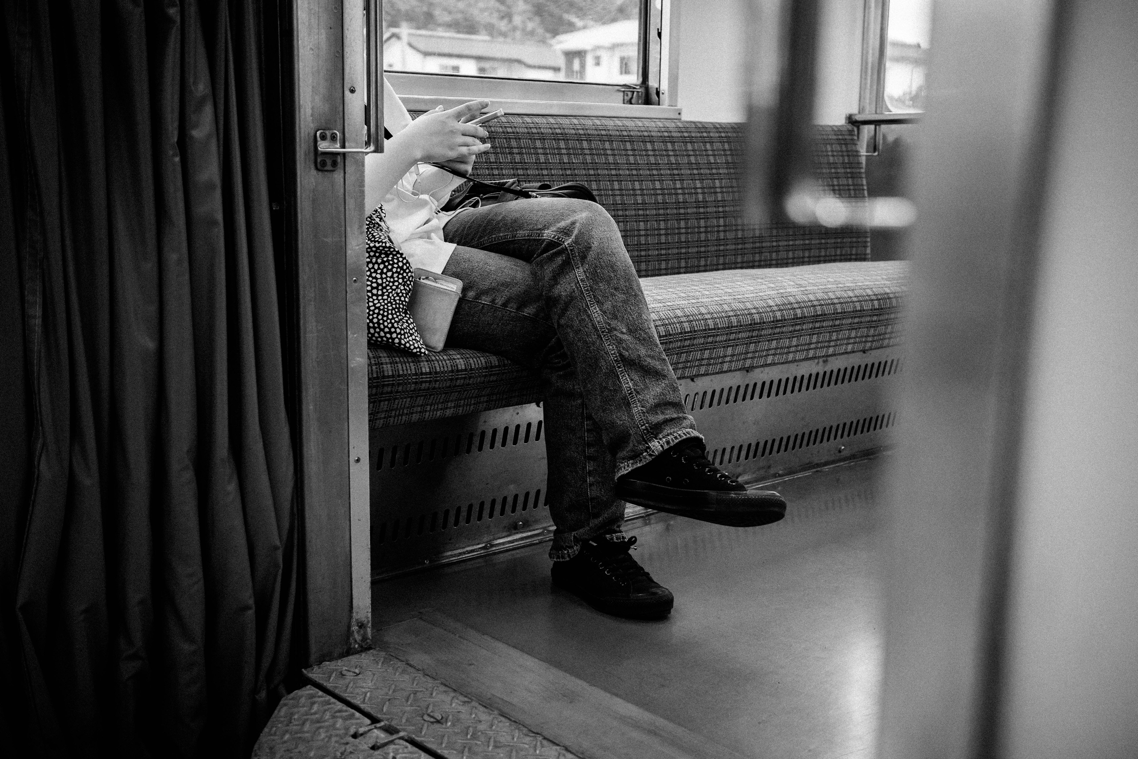 Una persona sentada en un tren con piernas y manos visibles en blanco y negro