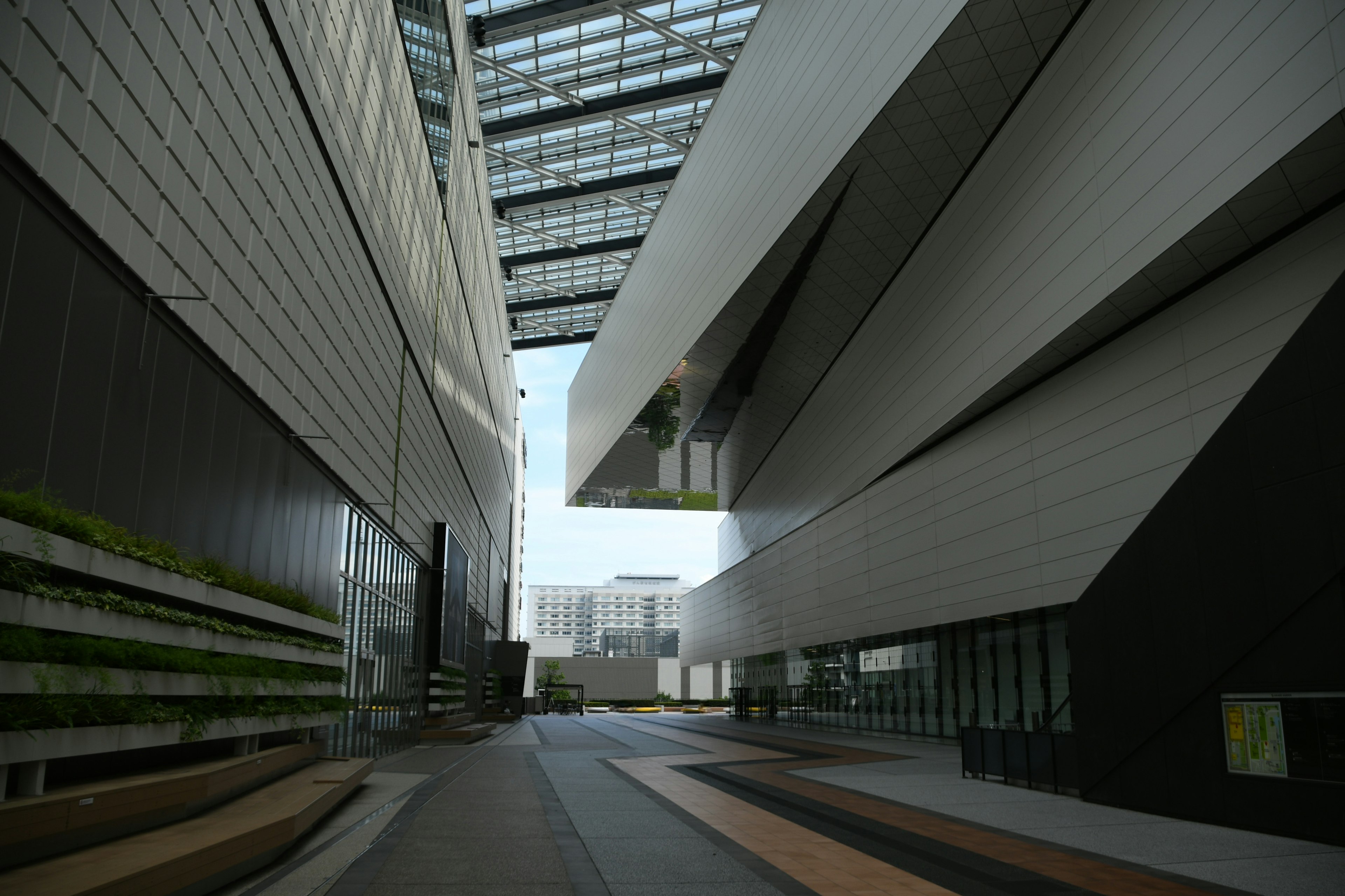 Passage between modern buildings featuring angled walls and glass facades